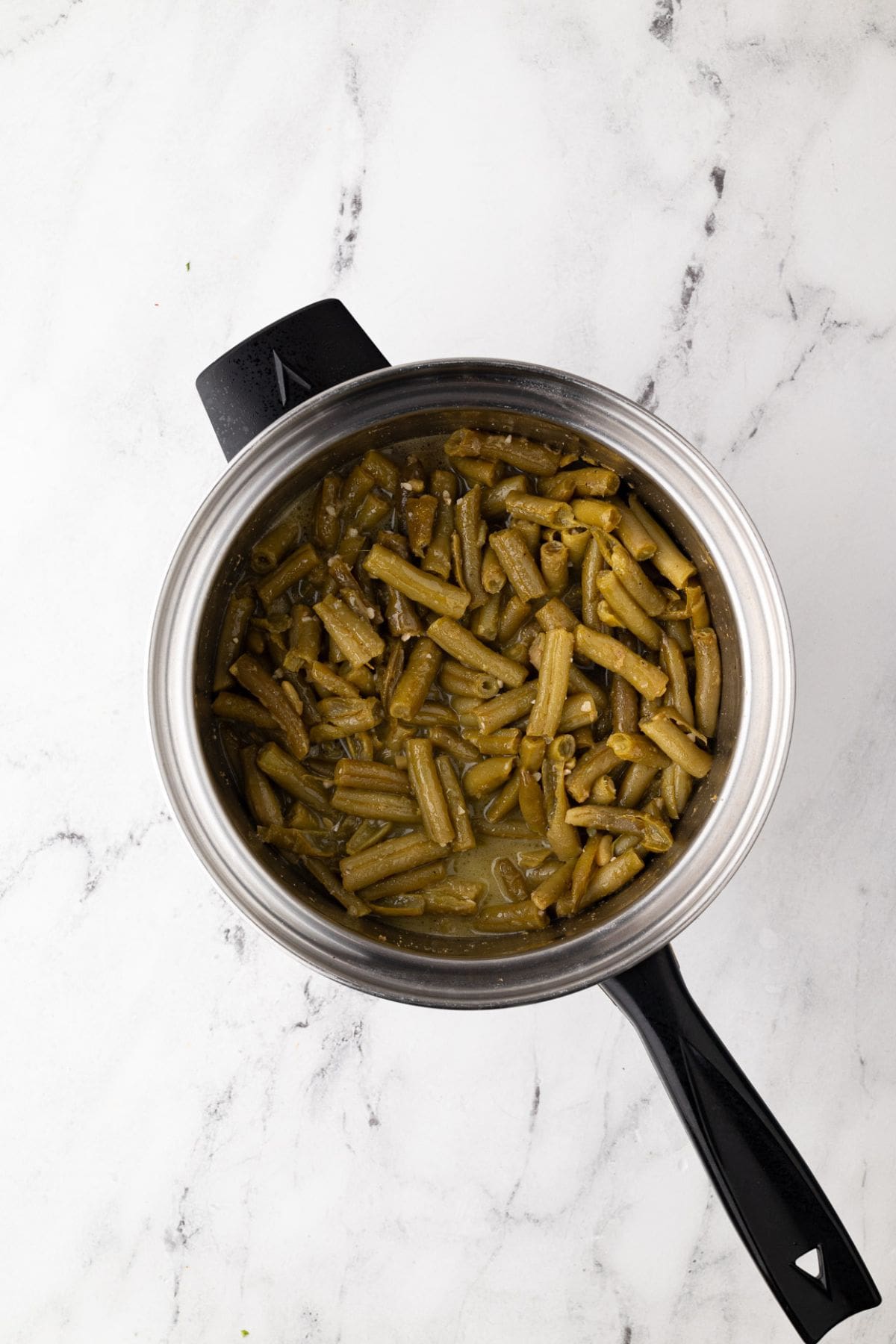 Overhead view of a pot of cooked green beans in their flavorful sauce.