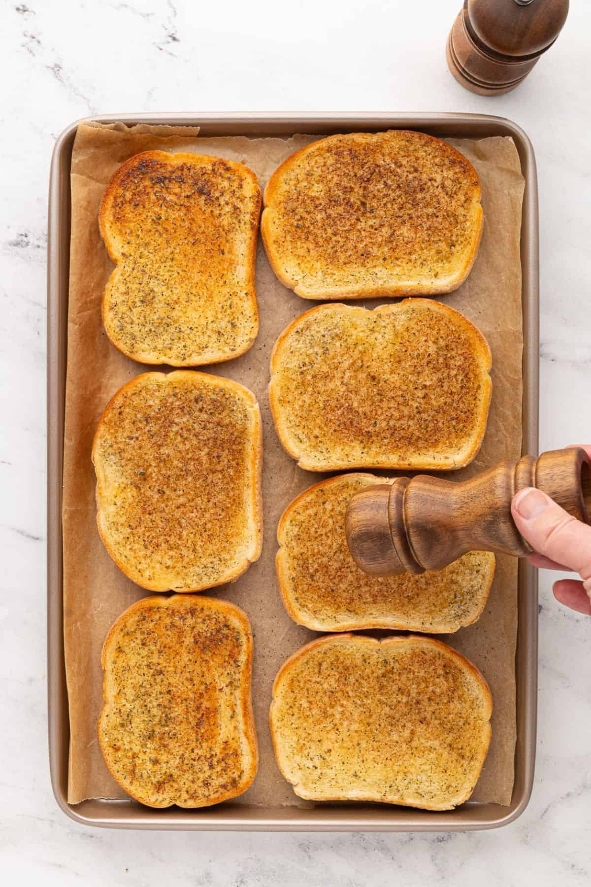Golden, toasted garlic bread topped with seasoning, arranged on a parchment-lined baking sheet.