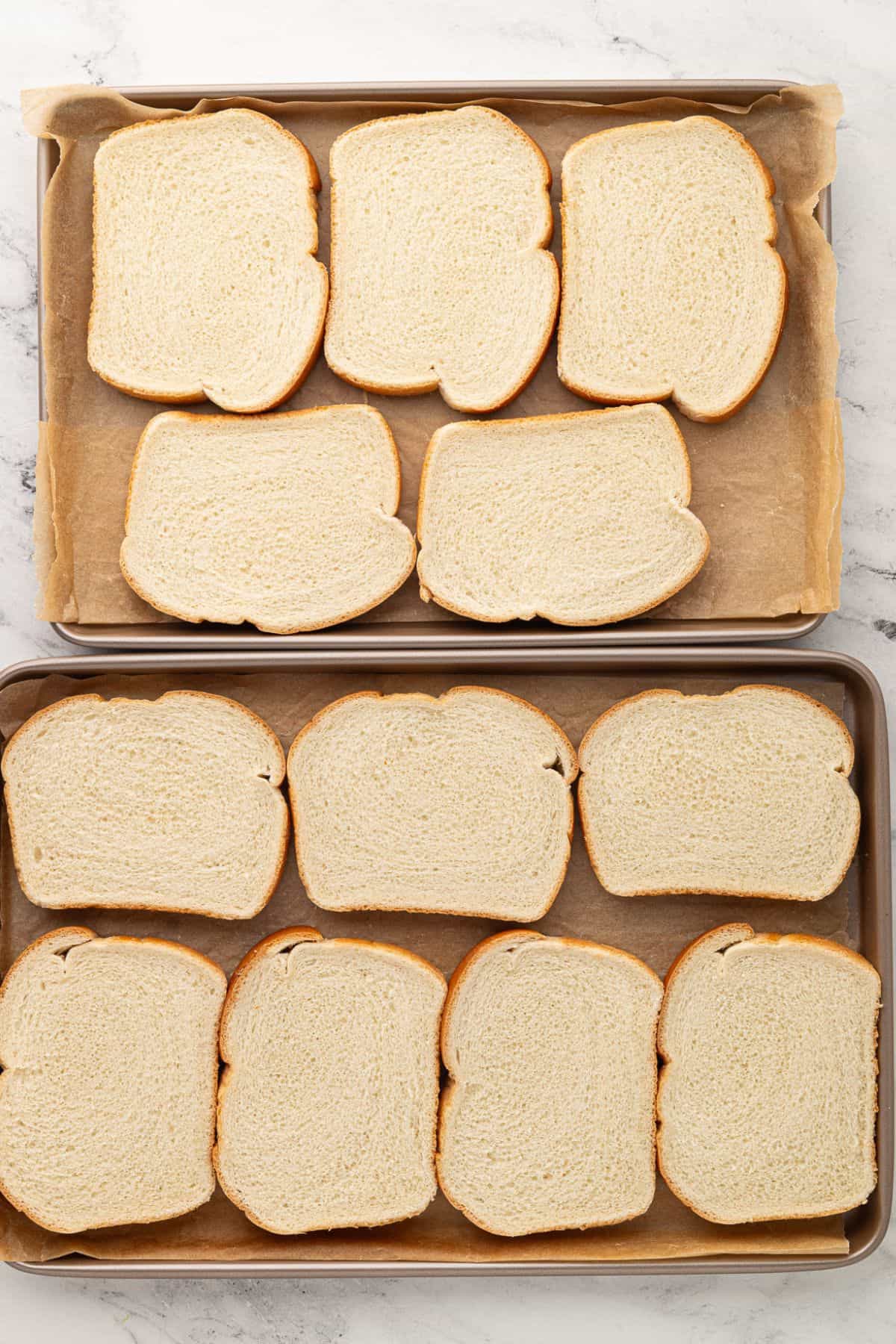 Plain bread slices arranged on parchment-lined baking sheets.