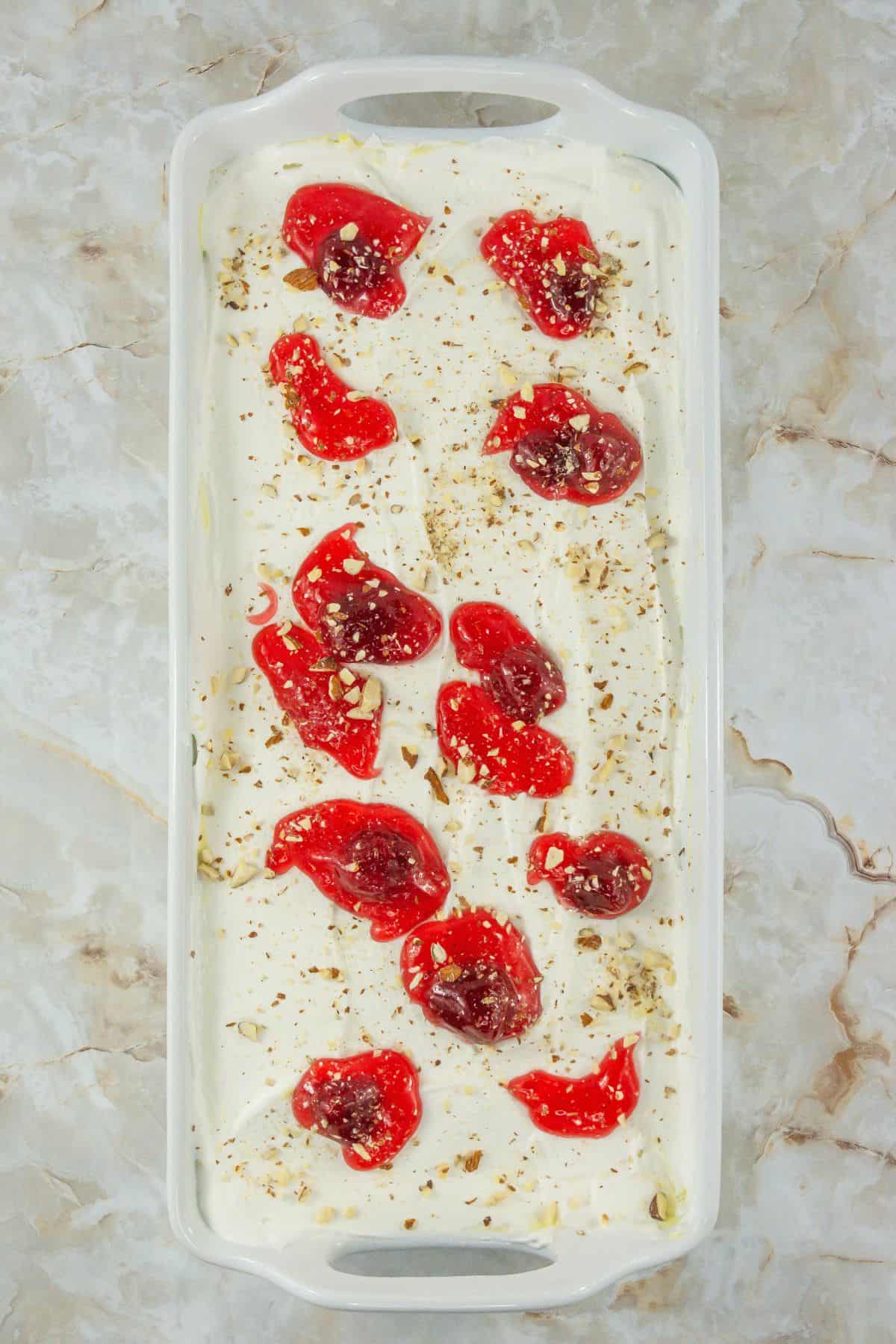 A cake topped with whipped cream, cherry pie filling, and sprinkled with nuts.