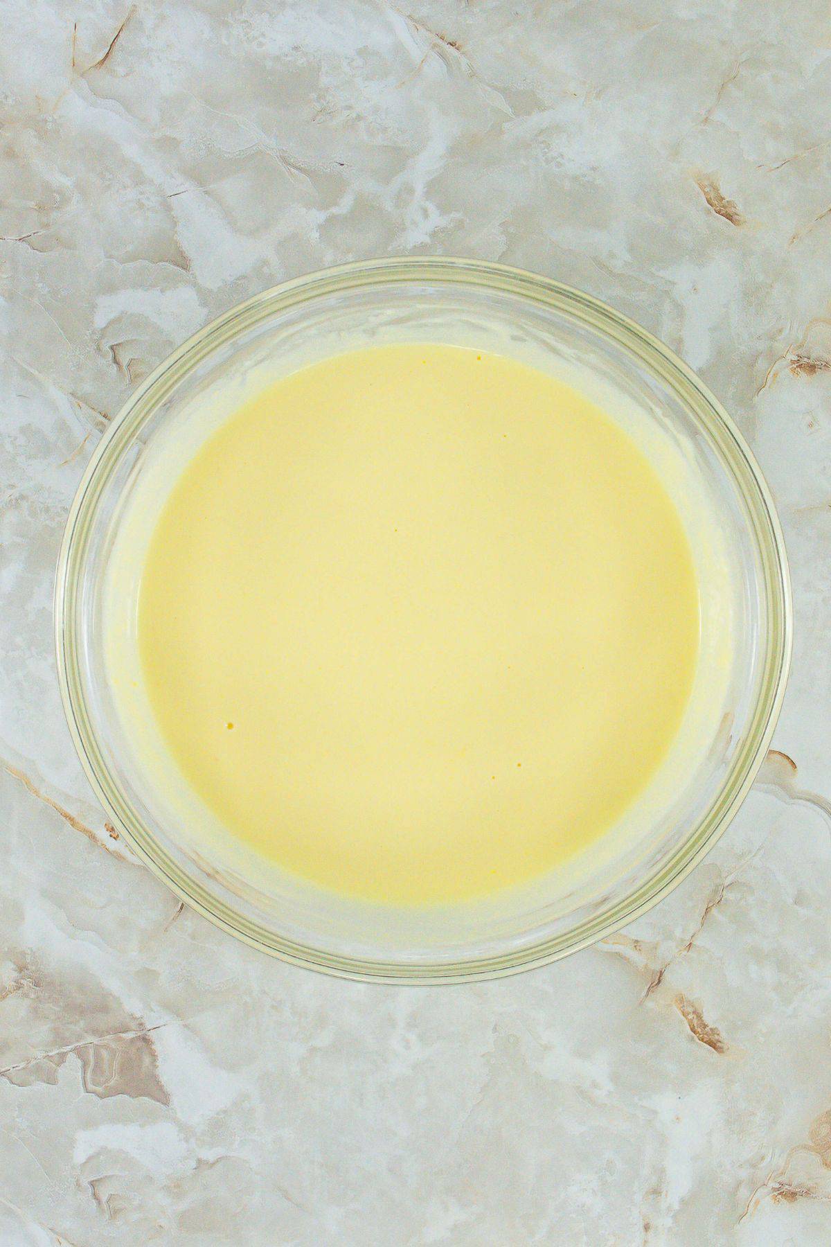 A bowl with smooth, mixed yellow pudding and cream.