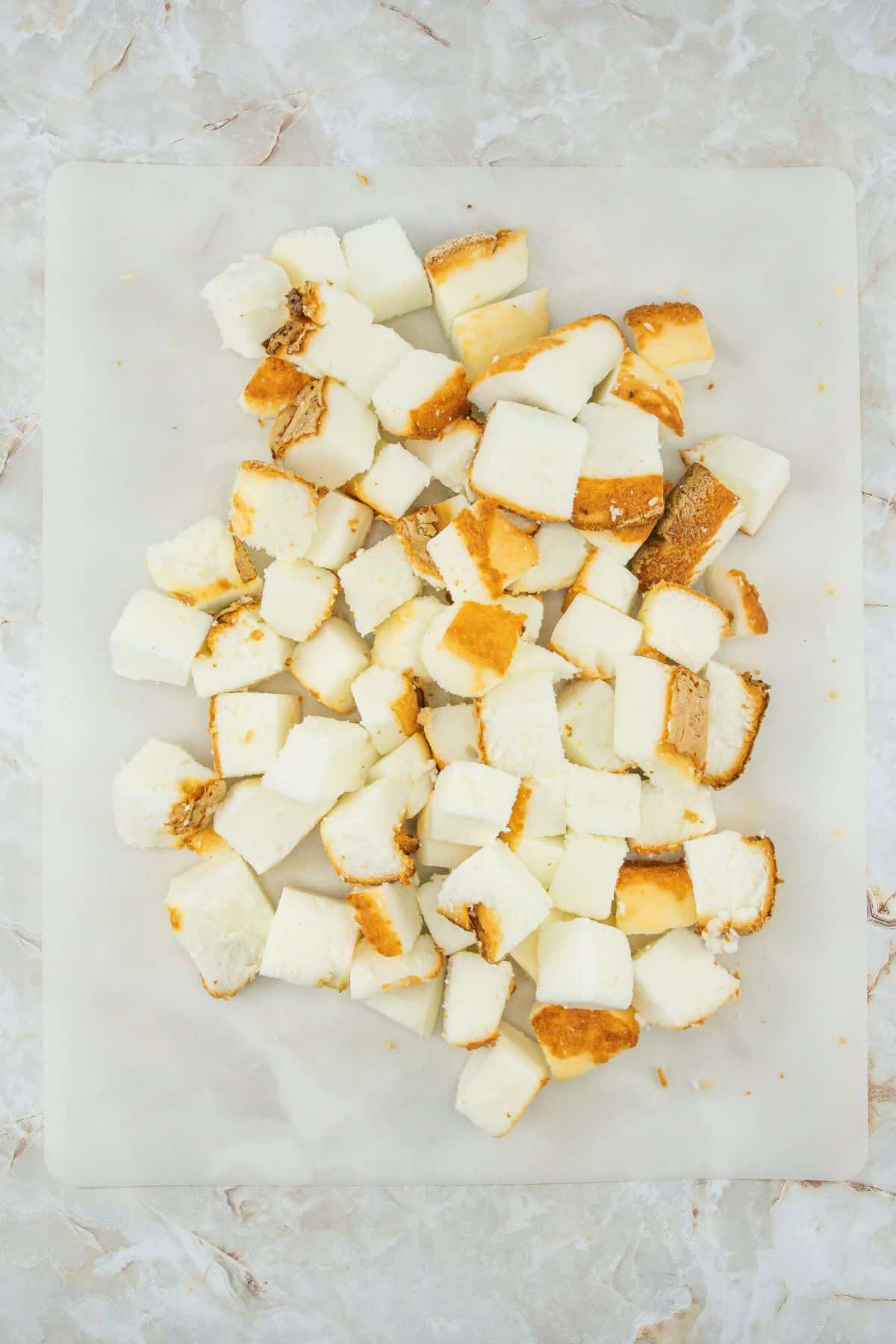 Cubed angel food cake pieces spread out on parchment paper.