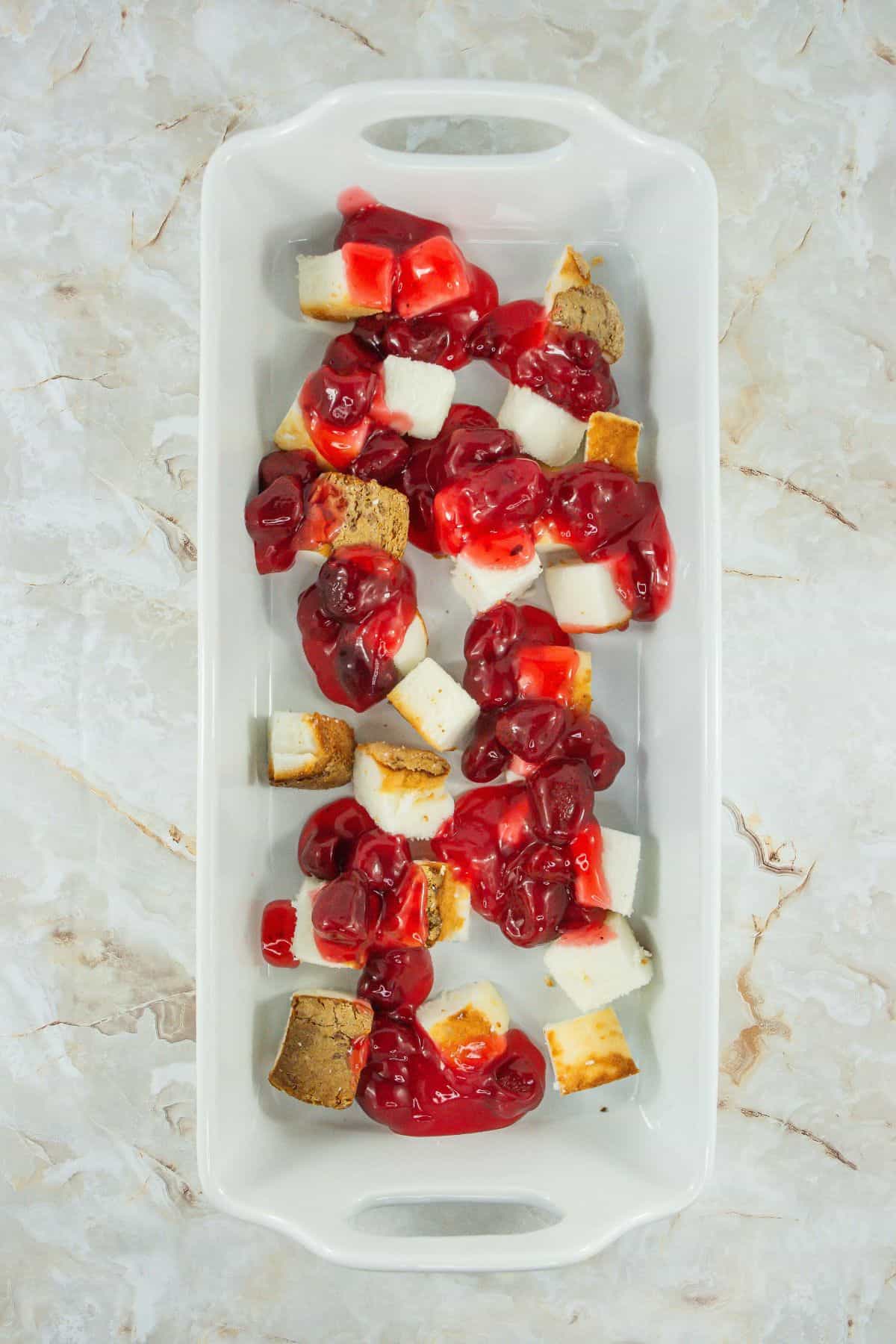 Cubed angel food cake in a dish covered with cherry pie filling.