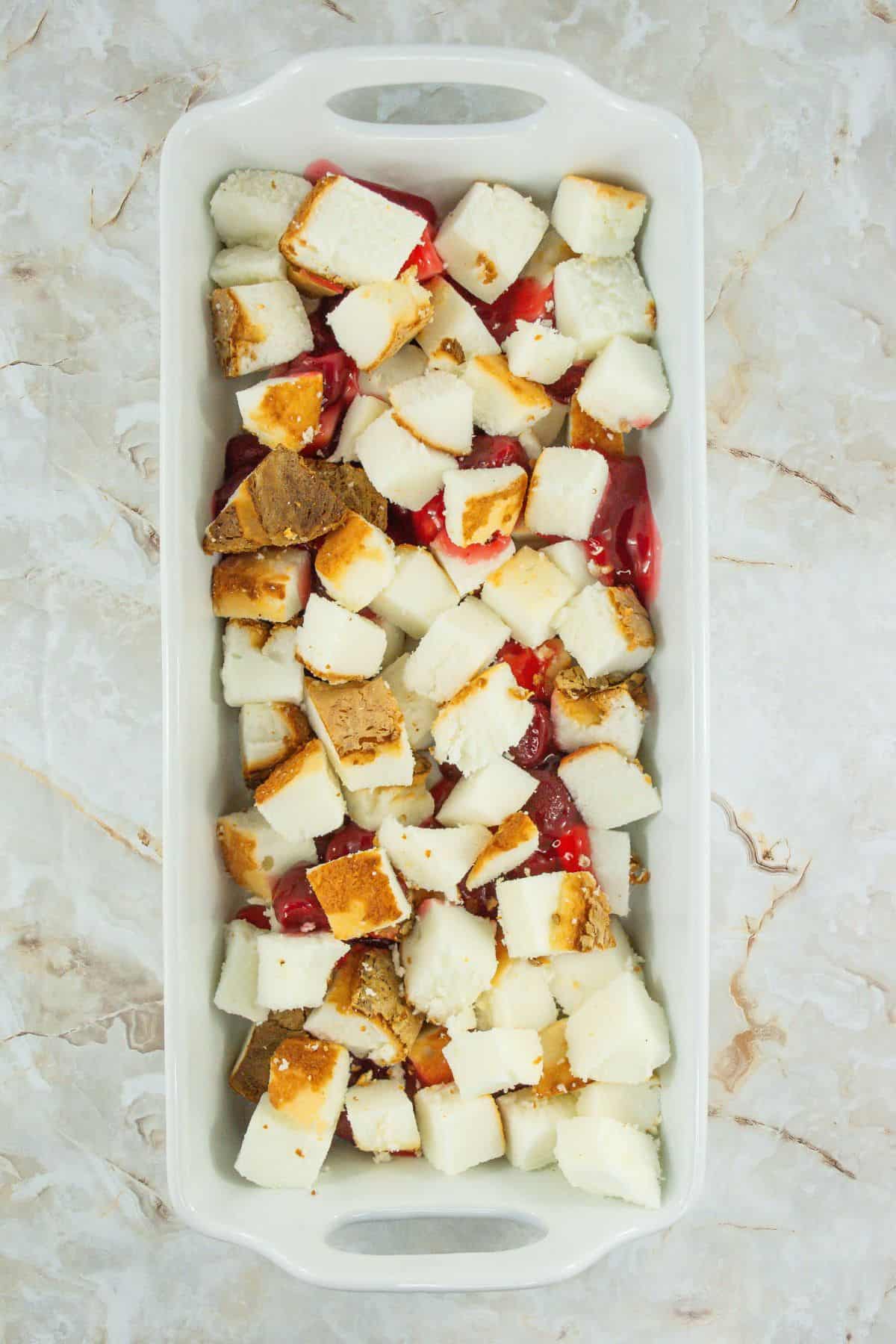 A baking dish filled with cubed angel food cake and cherry pie filling.