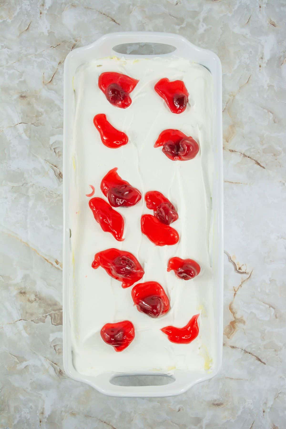 A baking dish with dessert layered in whipped cream and cherry topping.