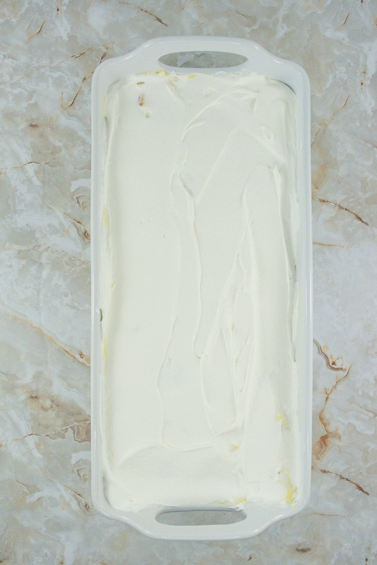 A baking dish with dessert covered completely in whipped cream, waiting for final toppings.