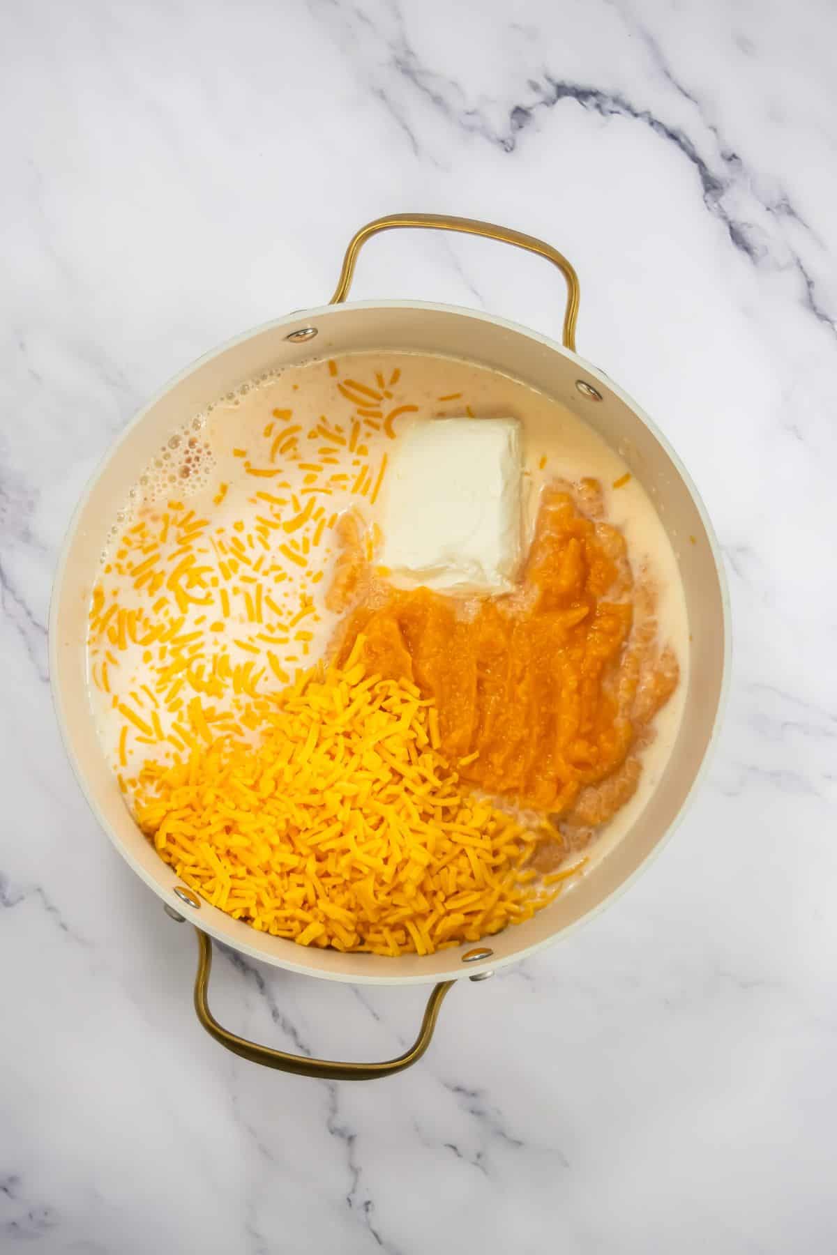 Ingredients in a pot: shredded cheese, cream cheese, and a puree of cooked vegetables ready to be mixed.