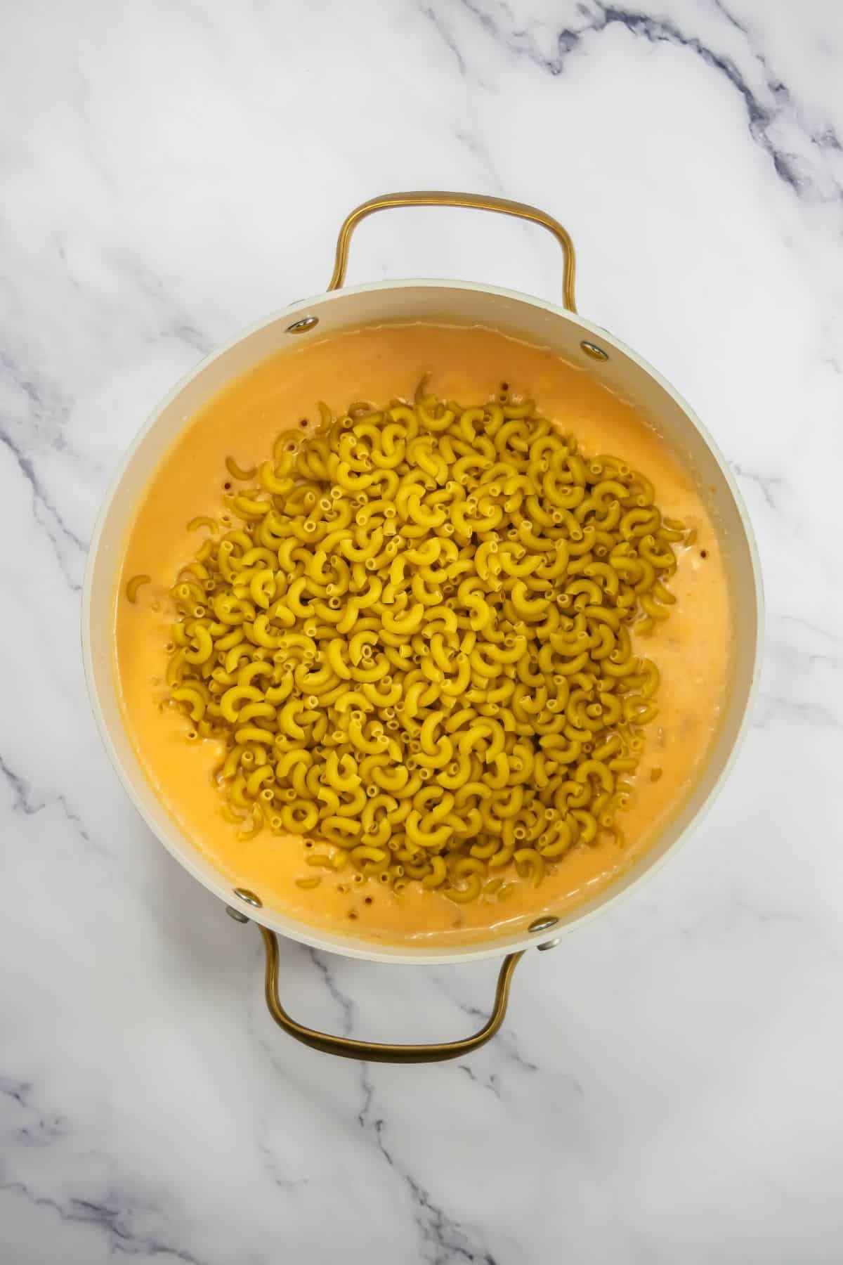 Dry macaroni added to the cheese sauce in a pot, showing the next step of preparation.