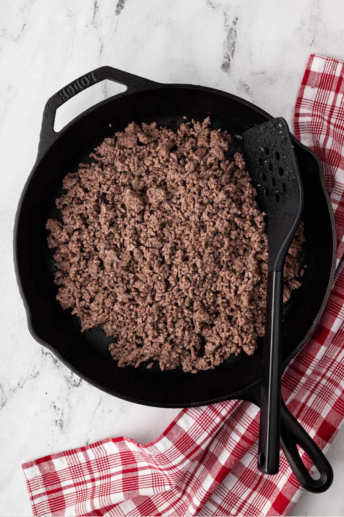 Ground beef is cooked in a cast iron skillet until browned.