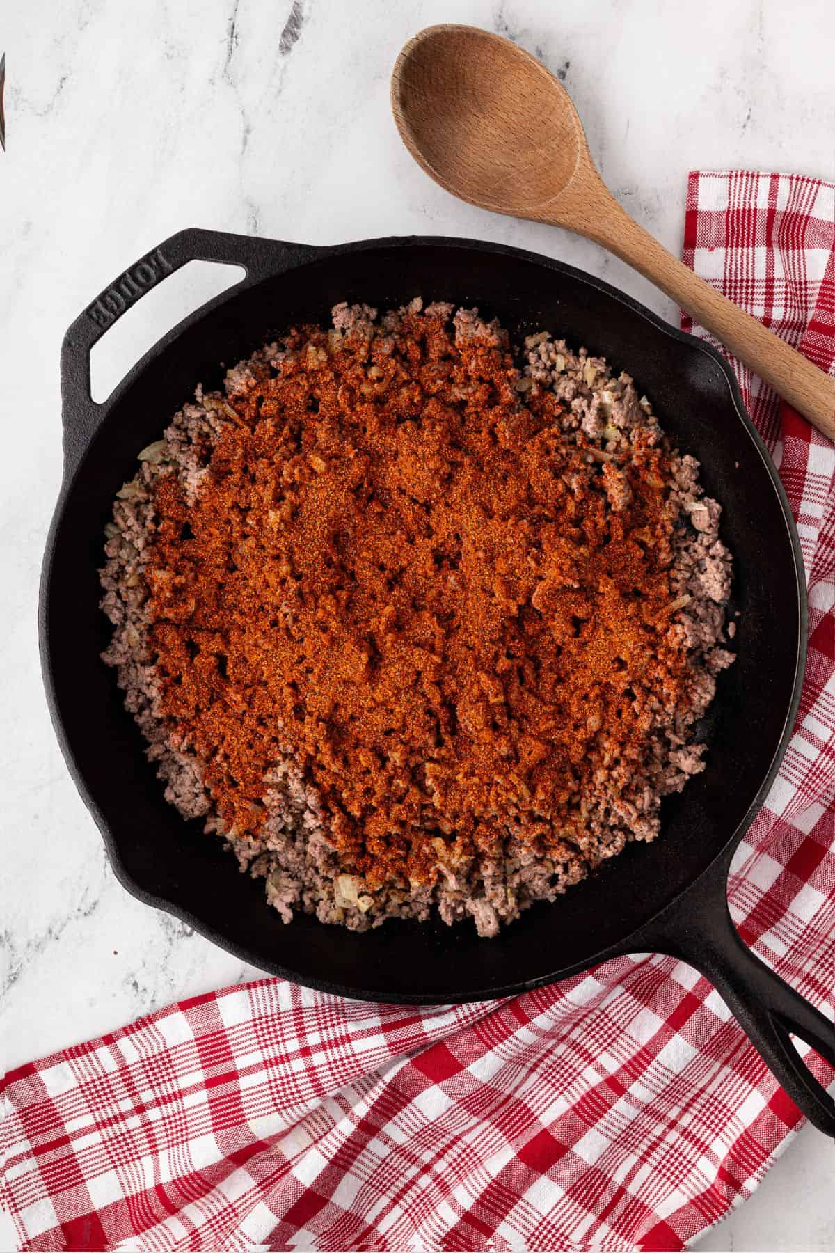 Chili seasoning is sprinkled over the cooked beef in the skillet.
