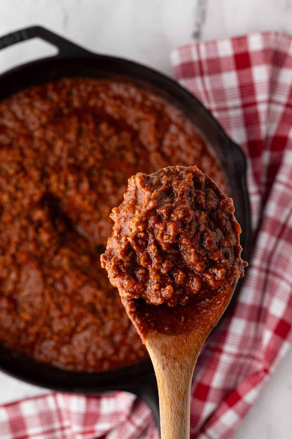 A wooden spoon scooping up thick, hearty chili from a cast iron skillet