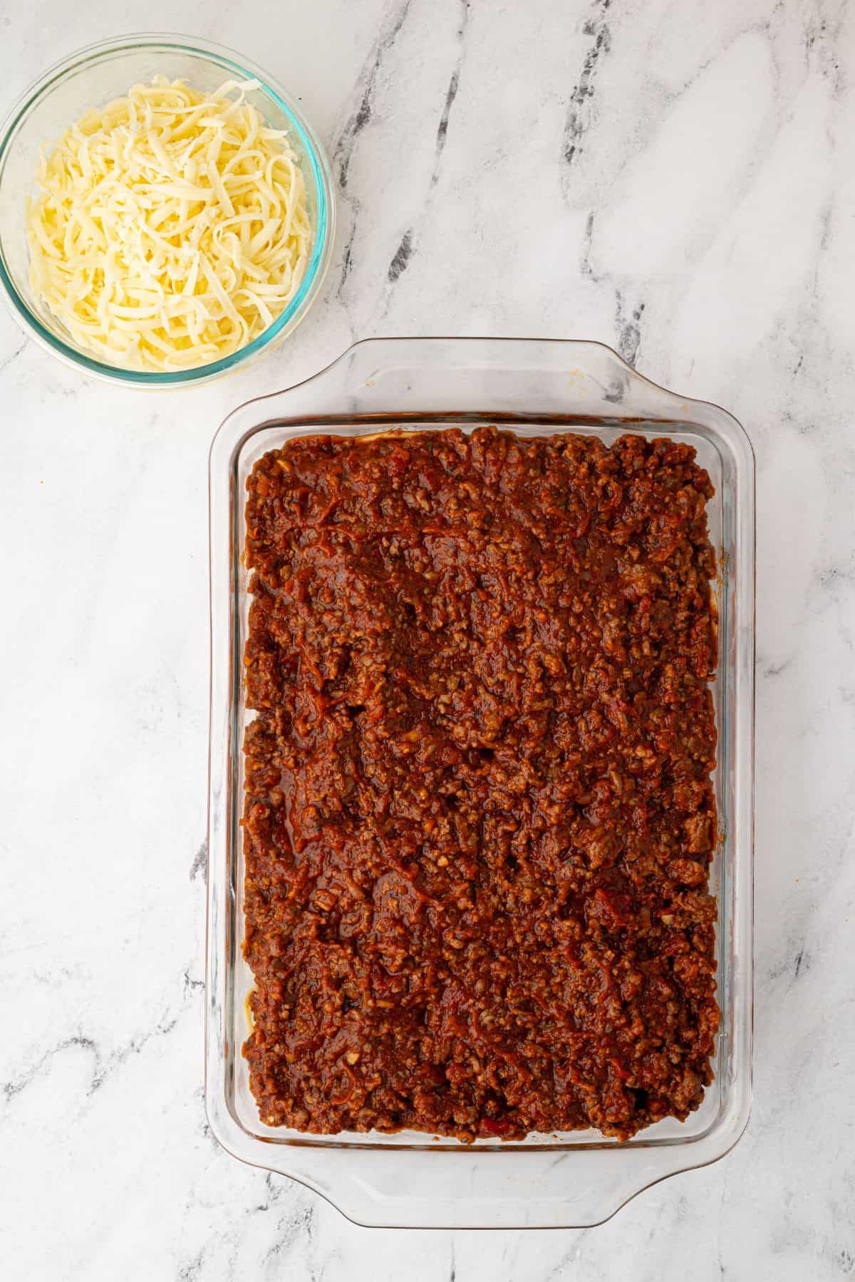 A glass baking dish with a layer of rich meat sauce spread over spaghetti.
