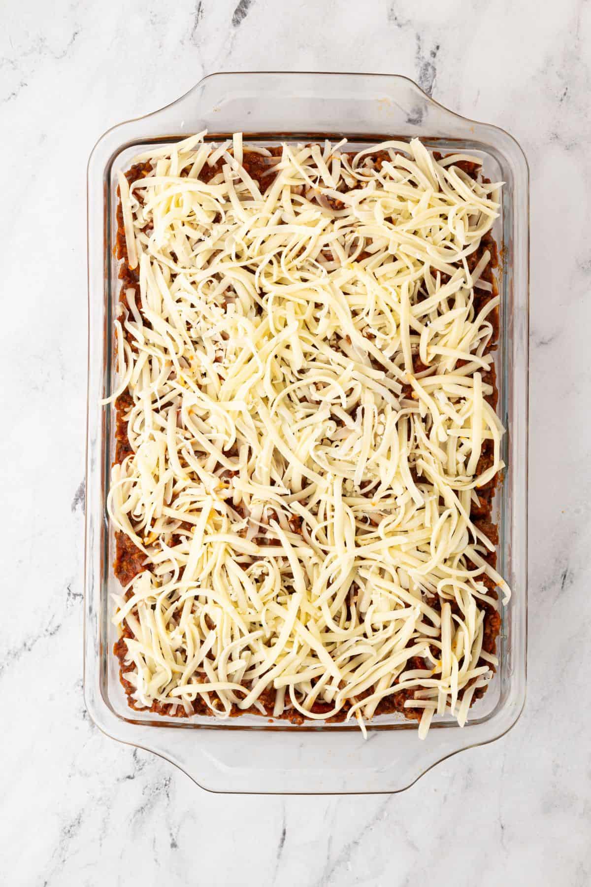 A baking dish with the final layer of shredded cheese before baking.