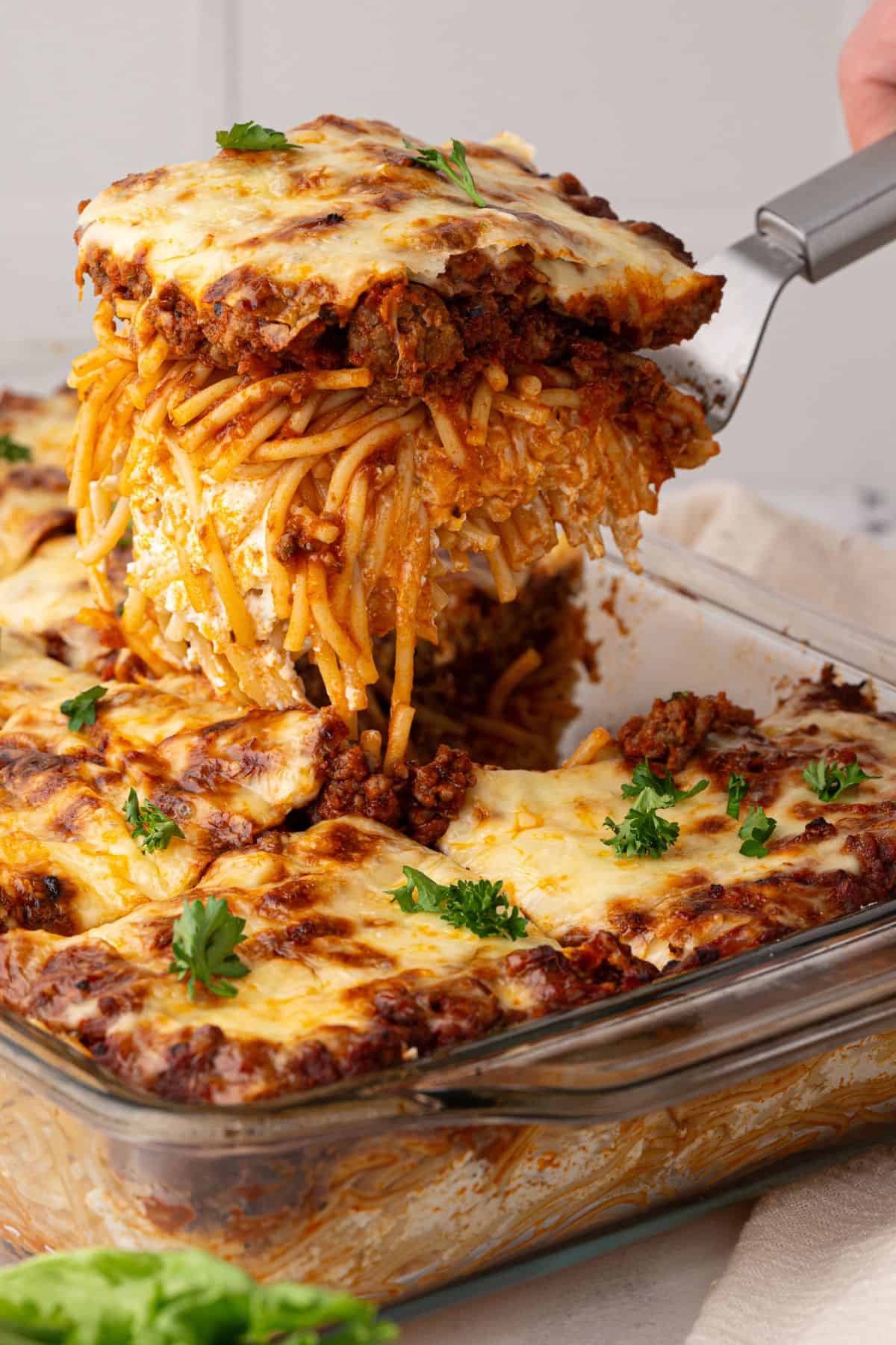 A spatula lifting a thick, cheesy slice of Million Dollar Spaghetti from the casserole dish.