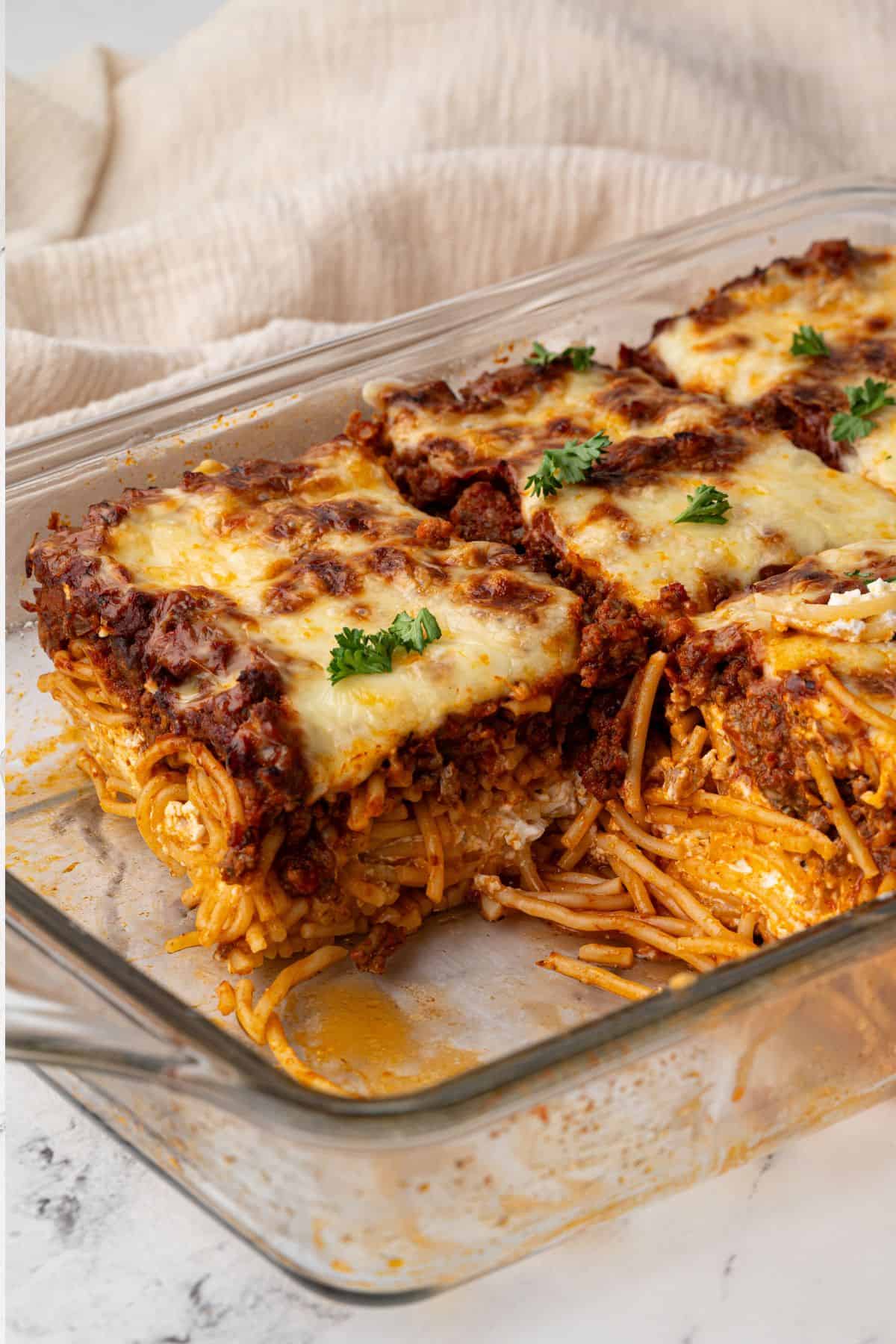 A close-up of a serving taken out of the casserole, showing layers of spaghetti, cheese, and meat sauce.