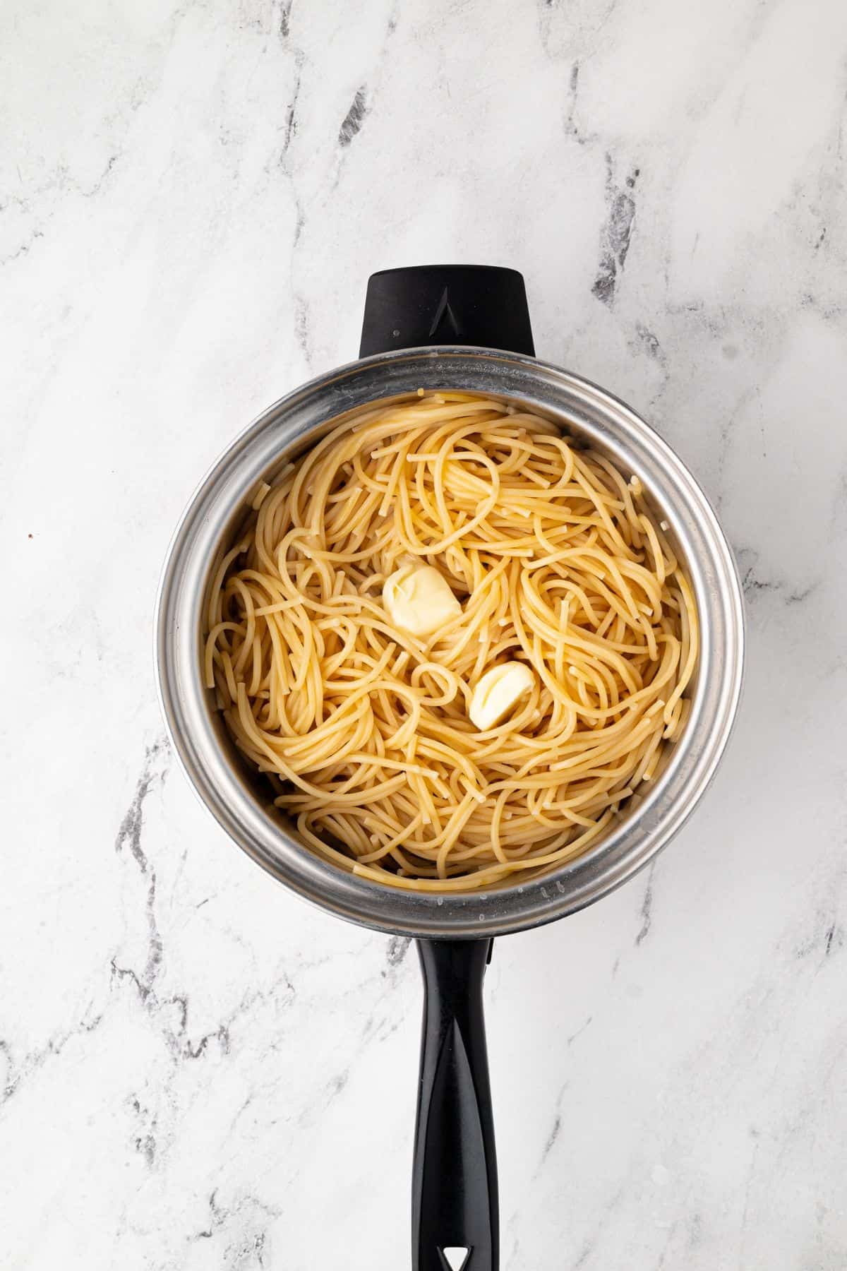 A pot of cooked spaghetti with butter melting on top.