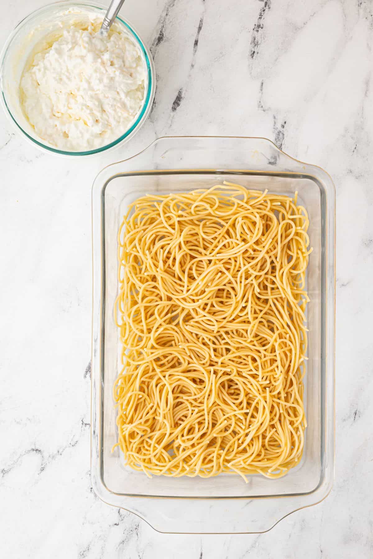 A glass baking dish filled with cooked spaghetti, ready for the next layers.