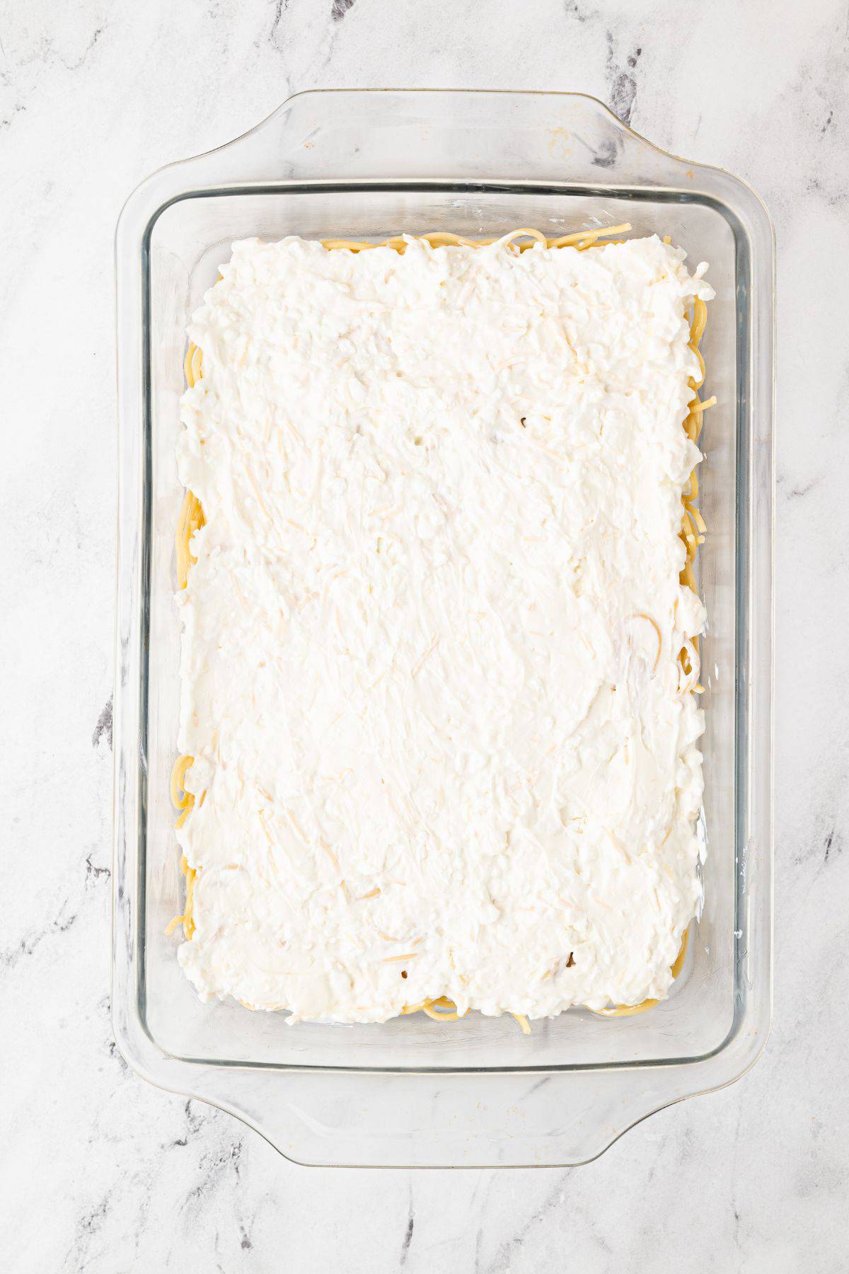 The cheese mixture spread evenly over the spaghetti in a casserole dish.