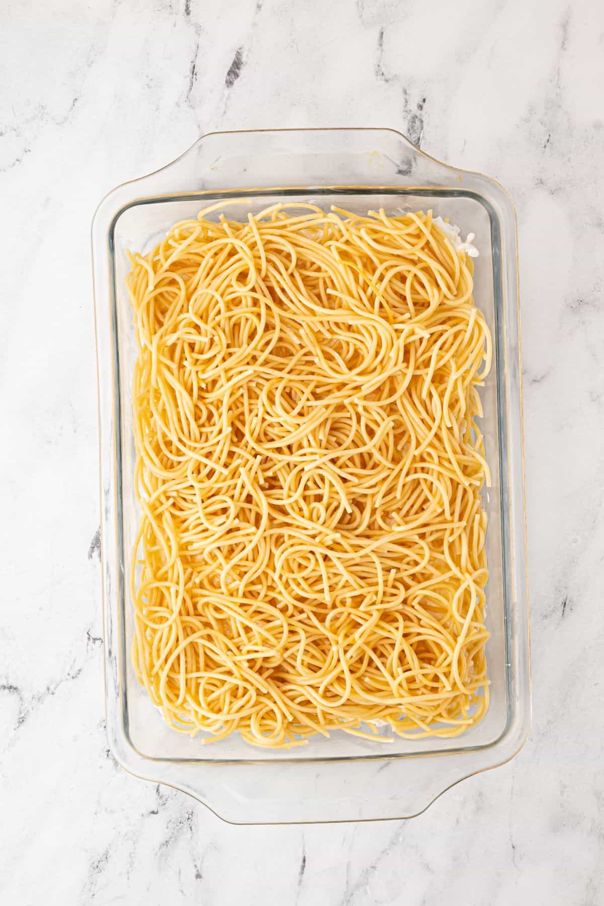 A glass baking dish with a layer of cooked spaghetti before other ingredients are added.