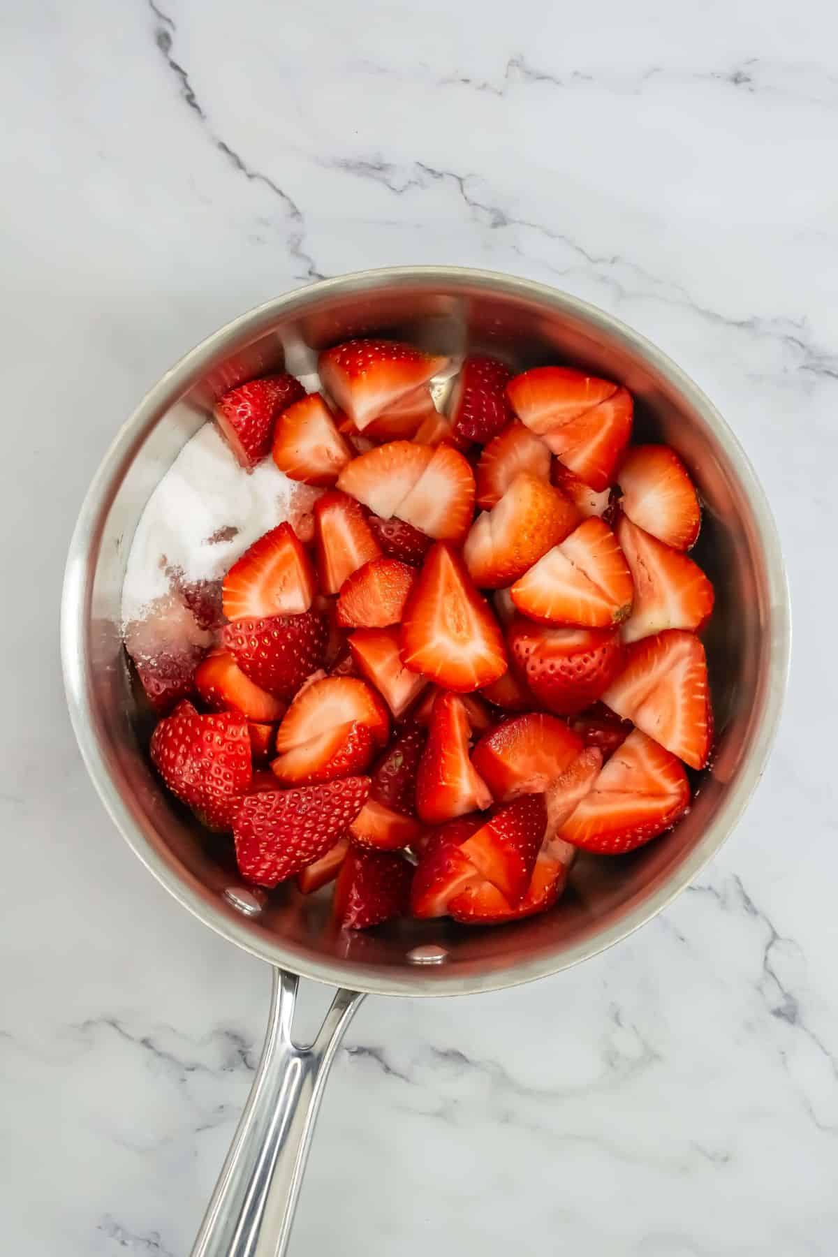 A saucepan with freshly chopped strawberries and sugar, ready to be cooked.