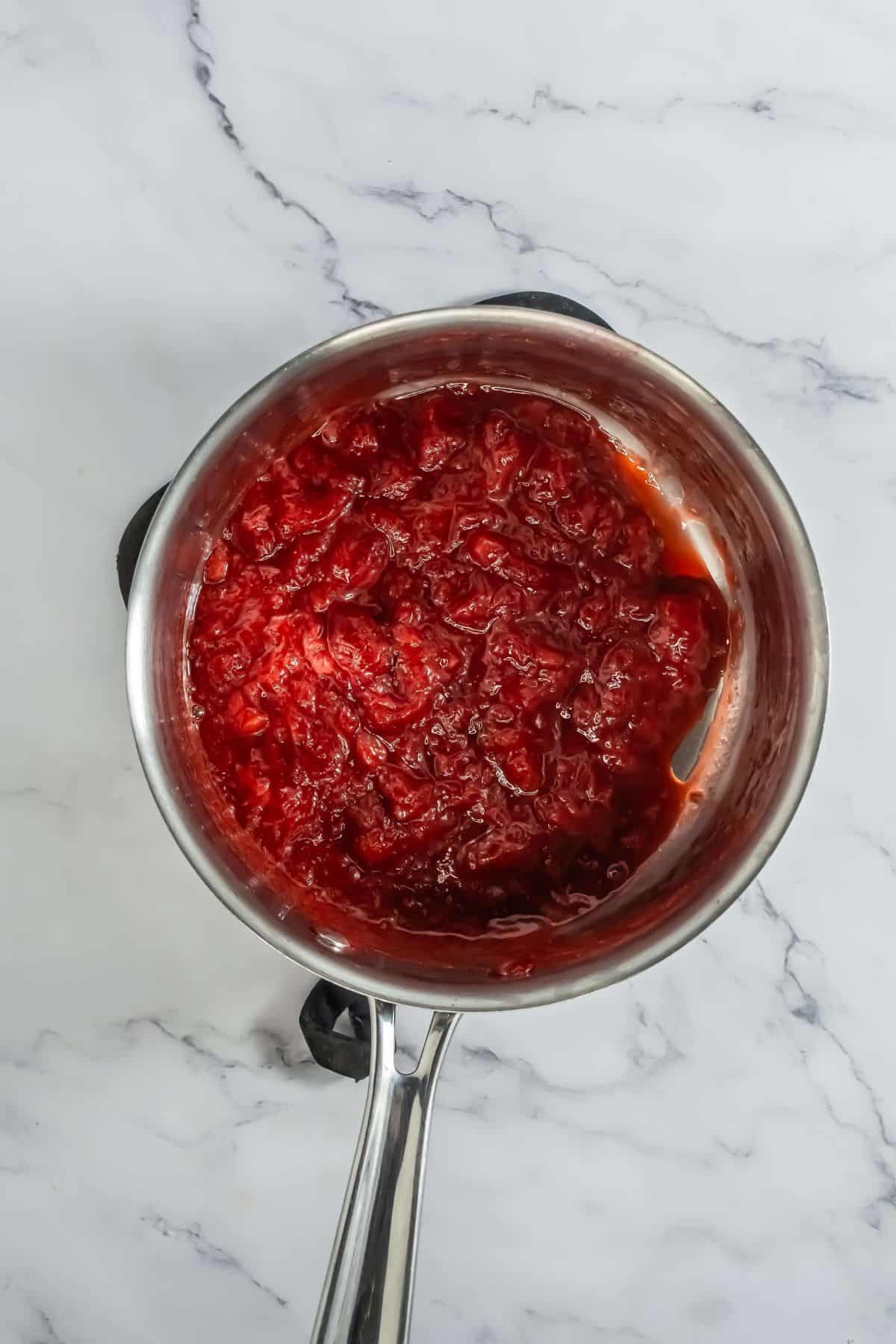 A saucepan filled with cooked, mashed strawberries, creating a thick strawberry compote.