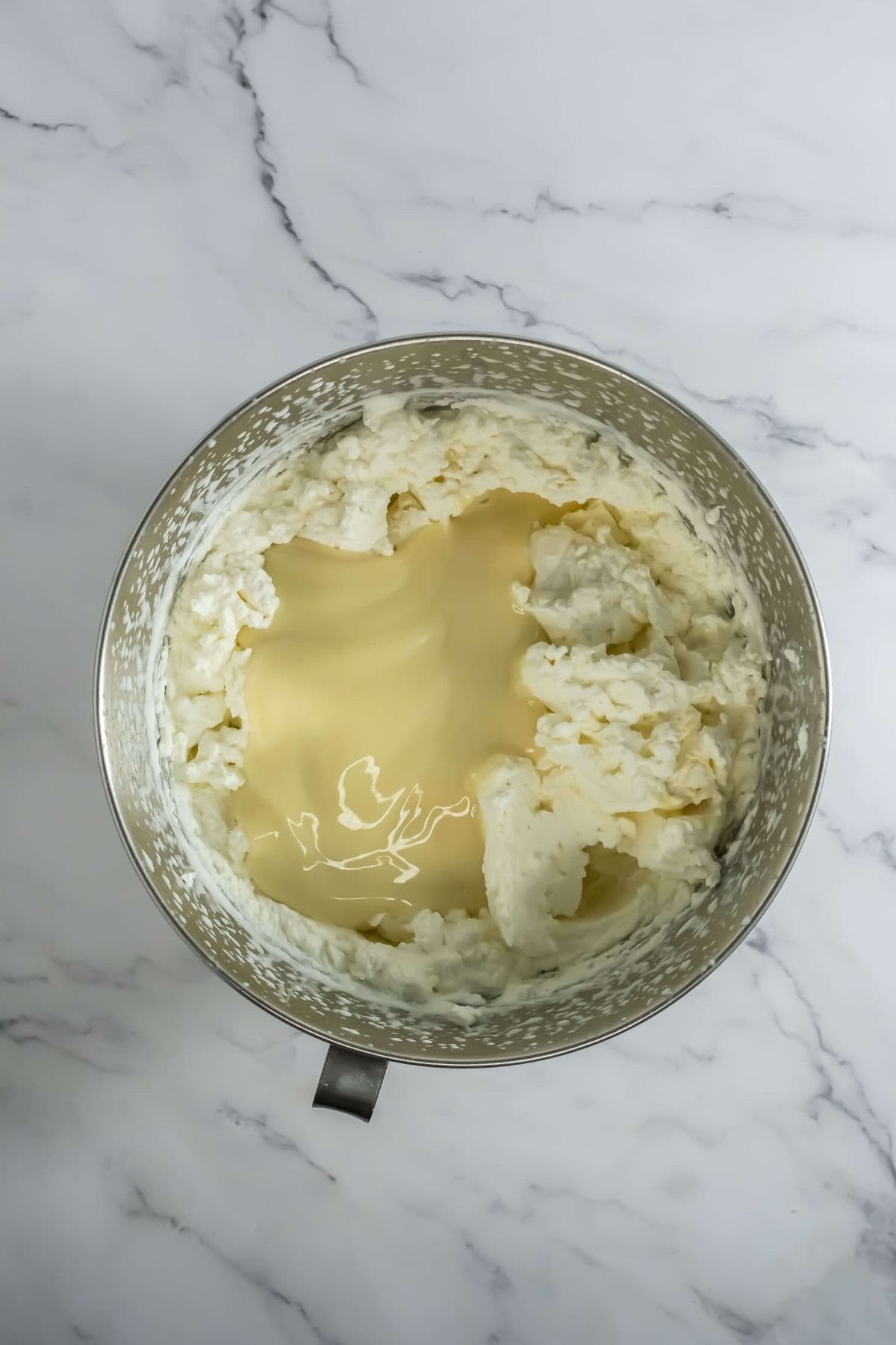 A mixing bowl with whipped cream combined with sweetened condensed milk.