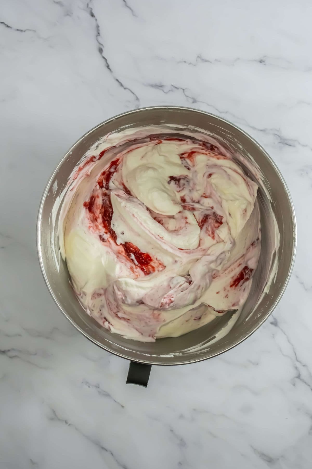 The whipped cream and strawberry compote partially swirled together in the bowl.