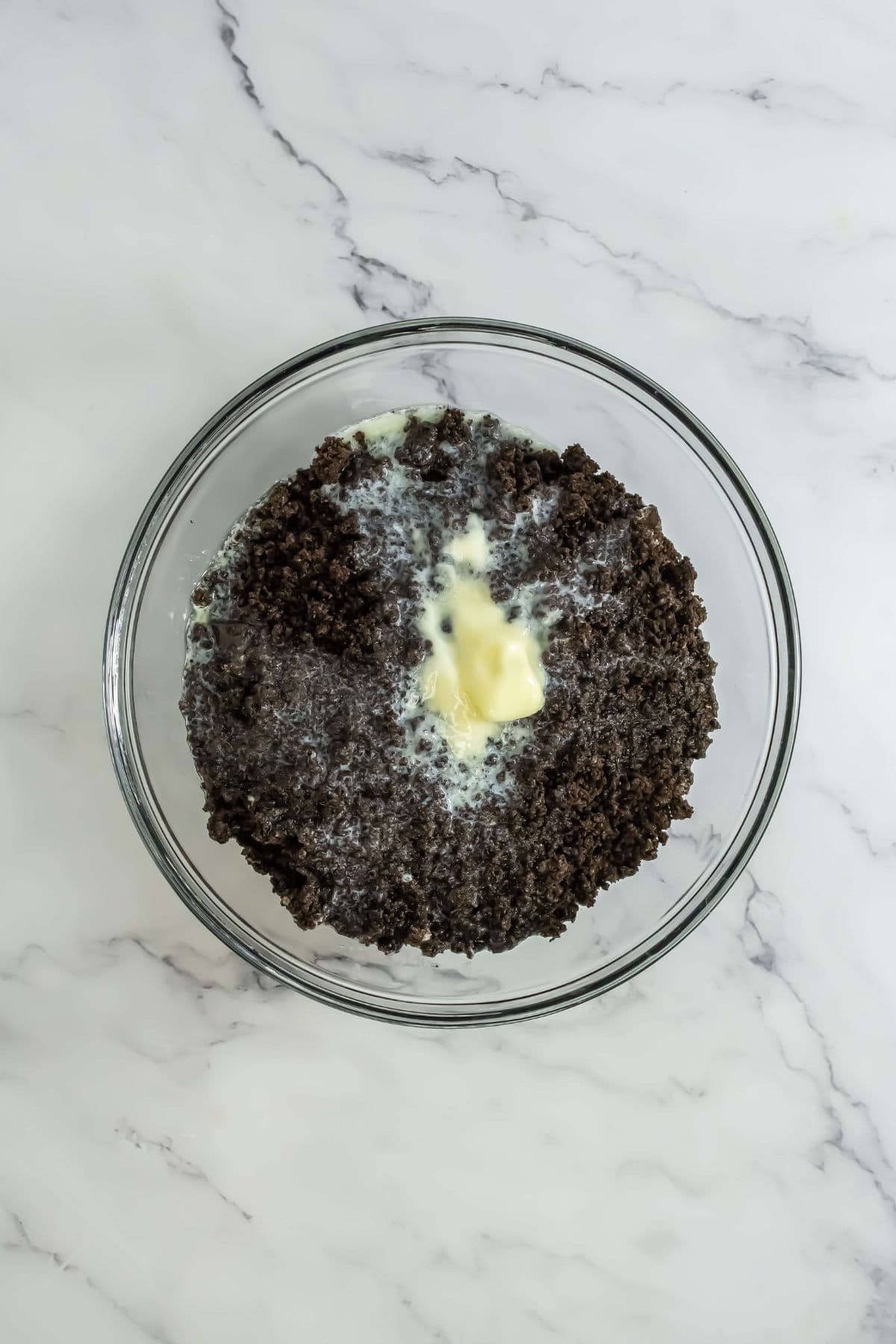 A glass bowl with crushed Oreos mixed with melted butter, ready to form the base.