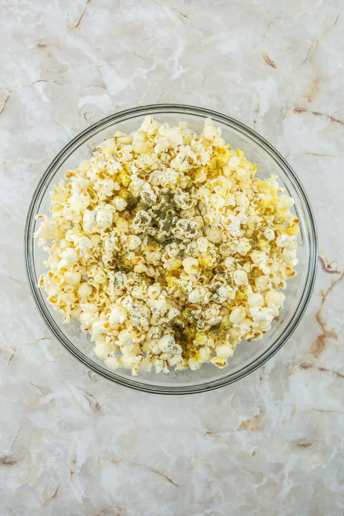 A bowl of popcorn with herb and seasoning sprinkled on top.