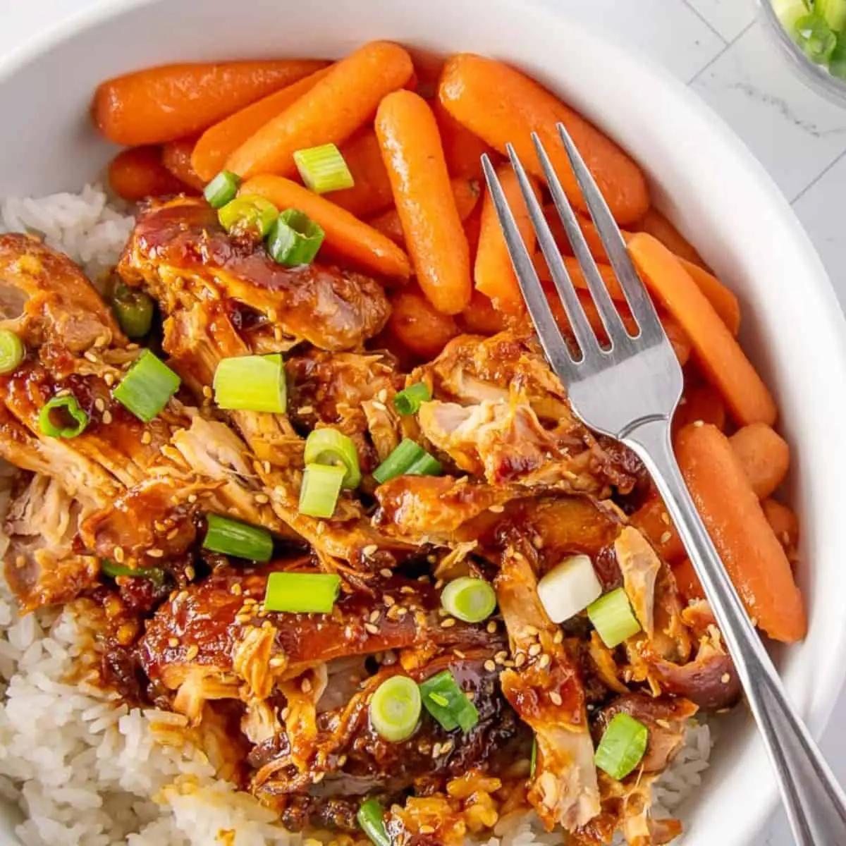 a bowl of slow cooker apricot chicken on a bed of rice with steamed carrots