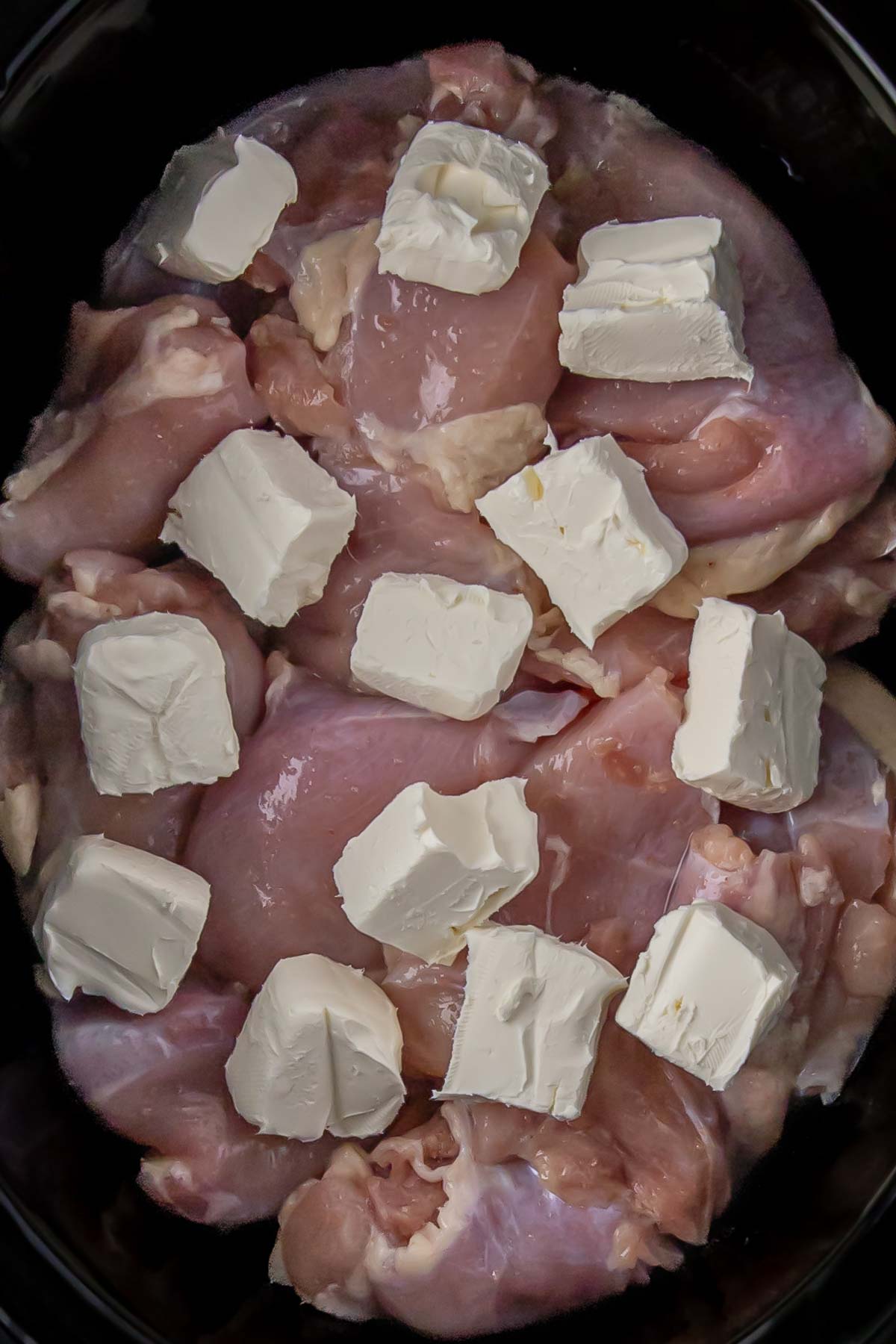 cream cheese cubes added to the seasoned chicken thighs in the slow cooker
