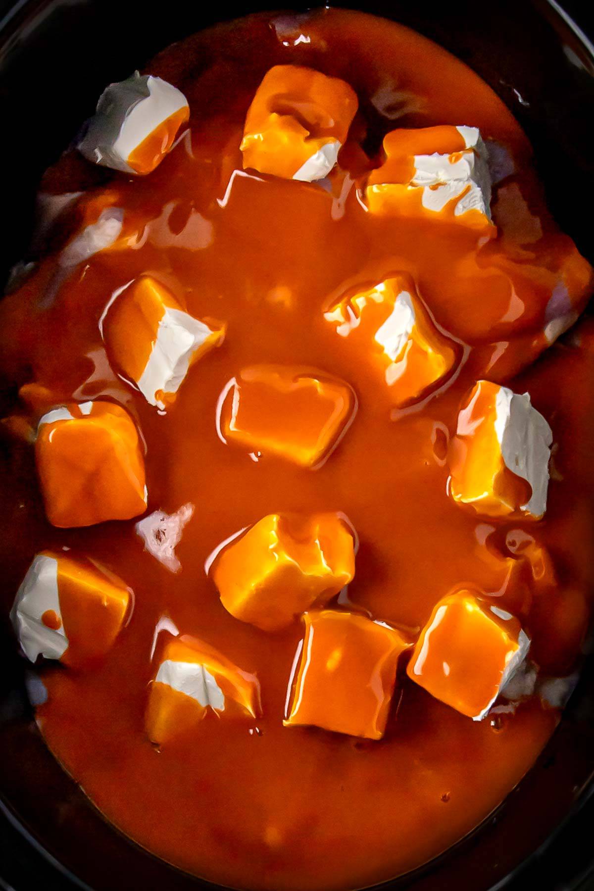 buffalo sauce added to the seasoned chicken thighs and cream cheese cubes in the slow cooker