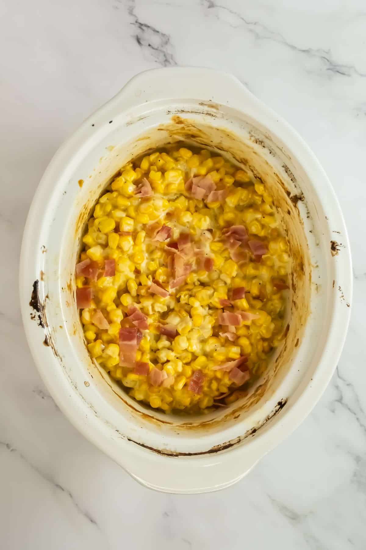 The finished creamy corn mixture garnished with bacon in the slow cooker.