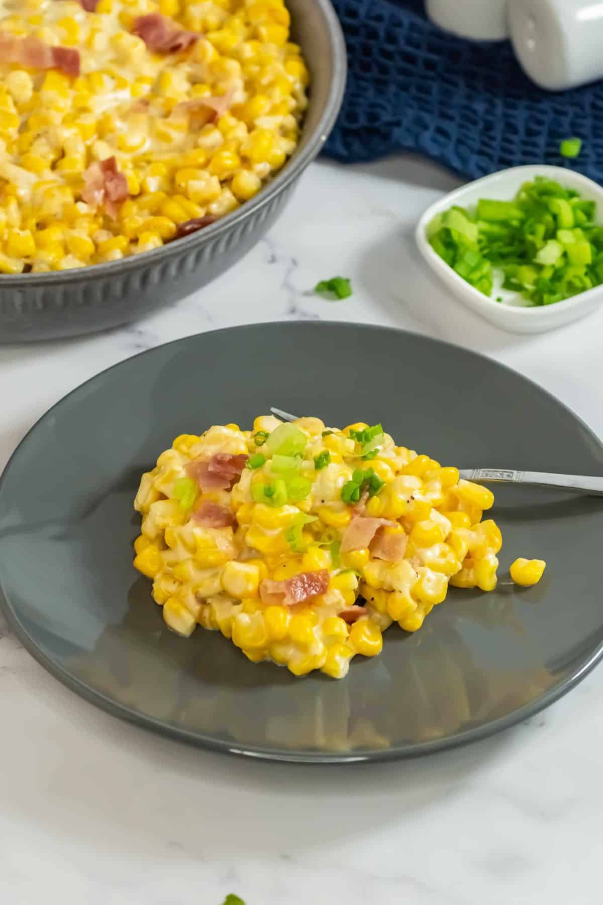 A large serving bowl full of creamy corn, garnished with bacon, ready to serve.