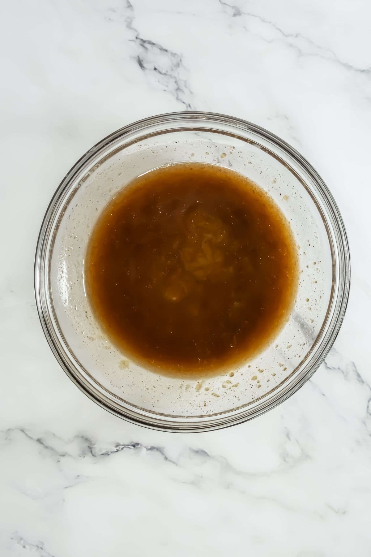 A close-up of a glass bowl filled with a brown glaze mixture. The texture appears smooth and glossy, showing the sauce before being combined with the carrots.