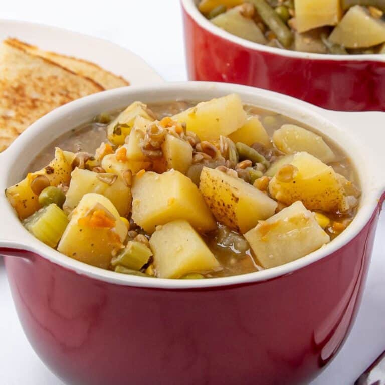 Slow cooker lentil stew in a red bowl with potatoes, lentils, broth, and frozen veggies
