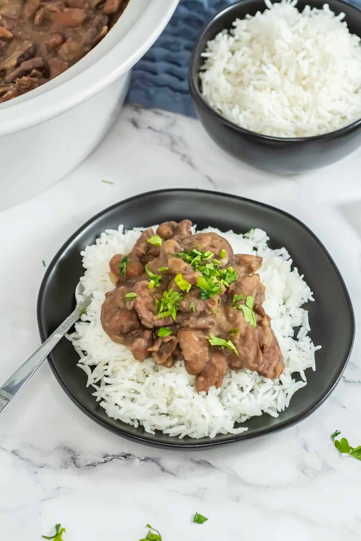Slow-cooked red beans and rice served on a black plate with parsley garnish.