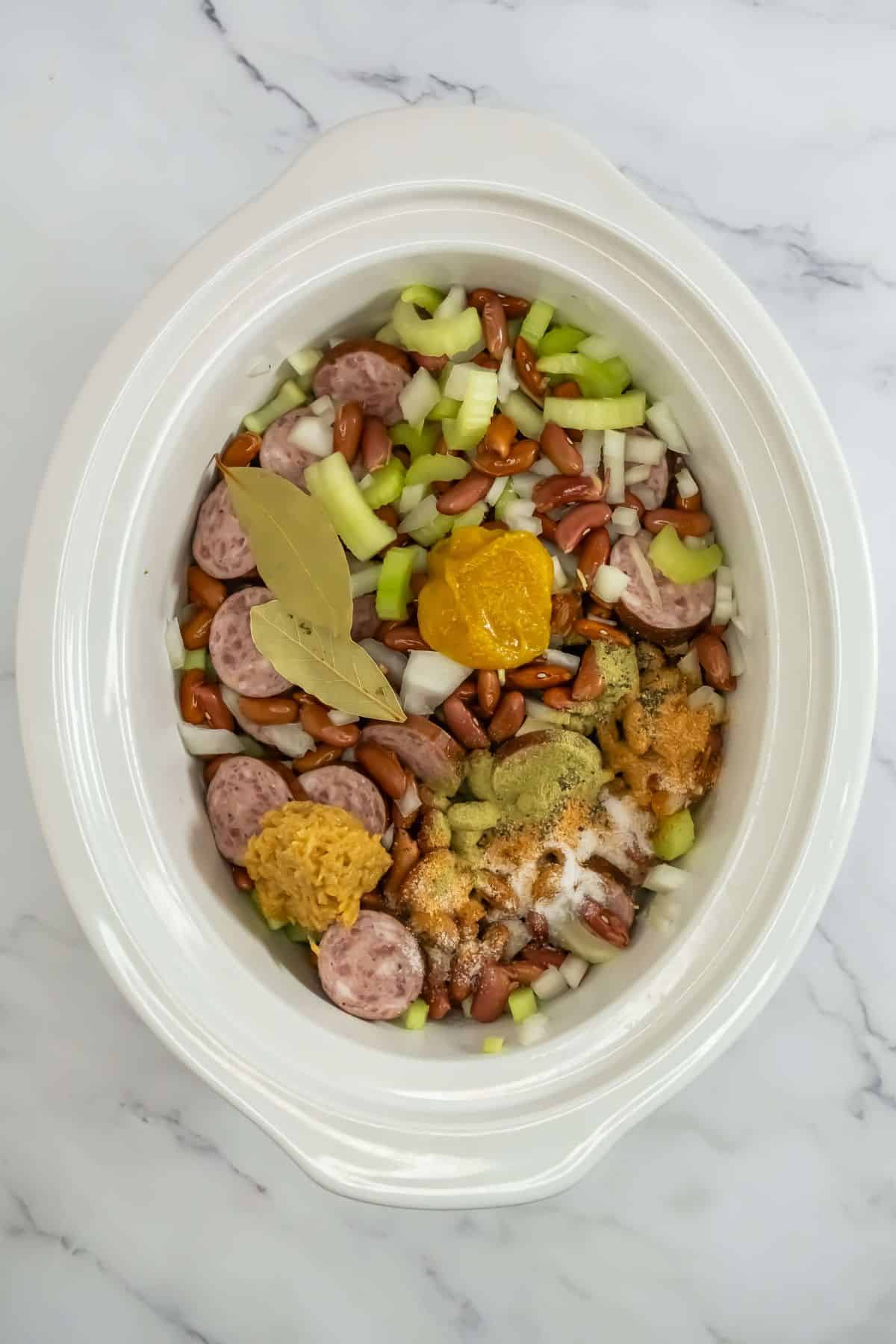 Ingredients, including sausages, celery, onions, and spices, in a slow cooker, ready to cook.