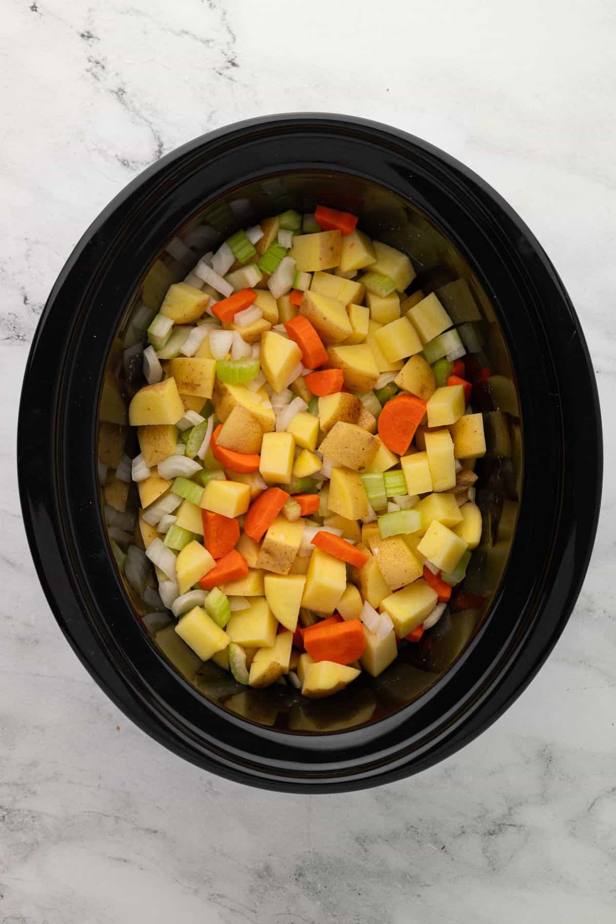 A mix of diced potatoes, carrots, celery, and onions neatly arranged in a slow cooker, ready for cooking.