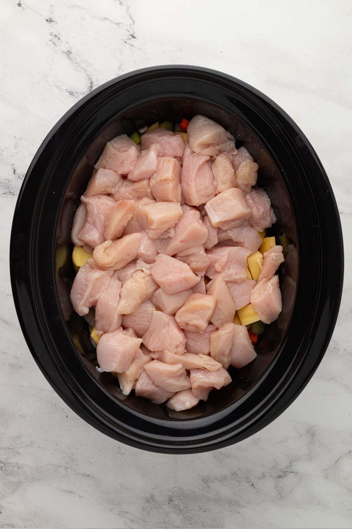 A slow cooker filled with colorful diced vegetables like potatoes, carrots, and celery.