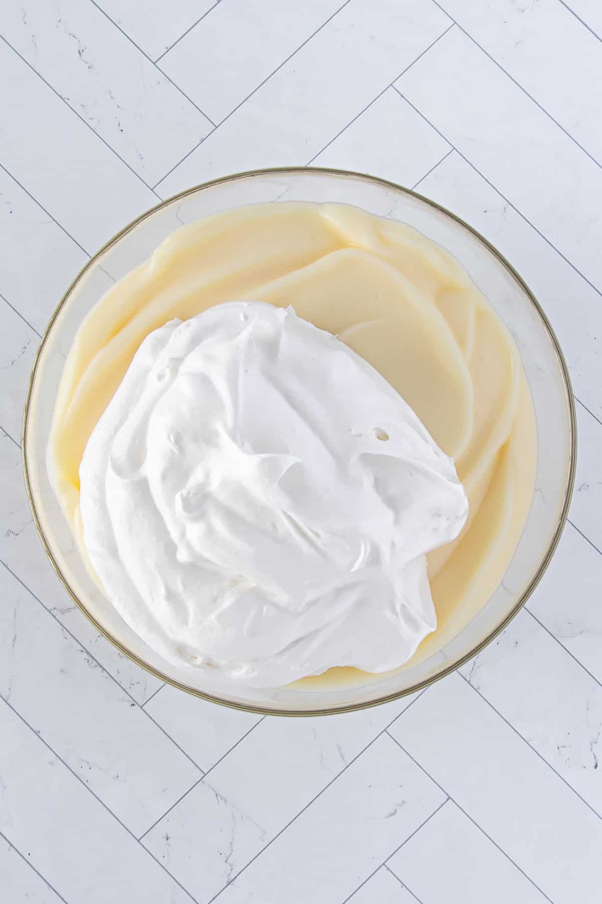 half of the whipped cream added to white chocolate pudding in a glass bowl