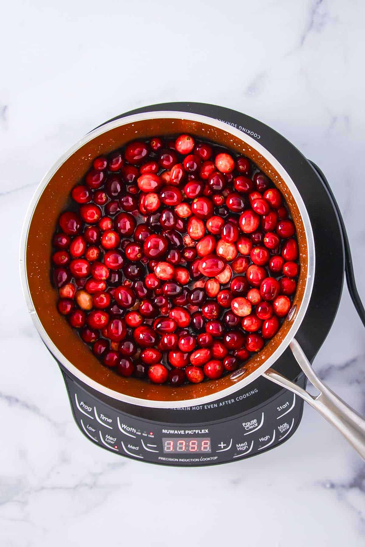 fresh cranberries added to dissolved sugar in water in a saucepan on an induction cooktop