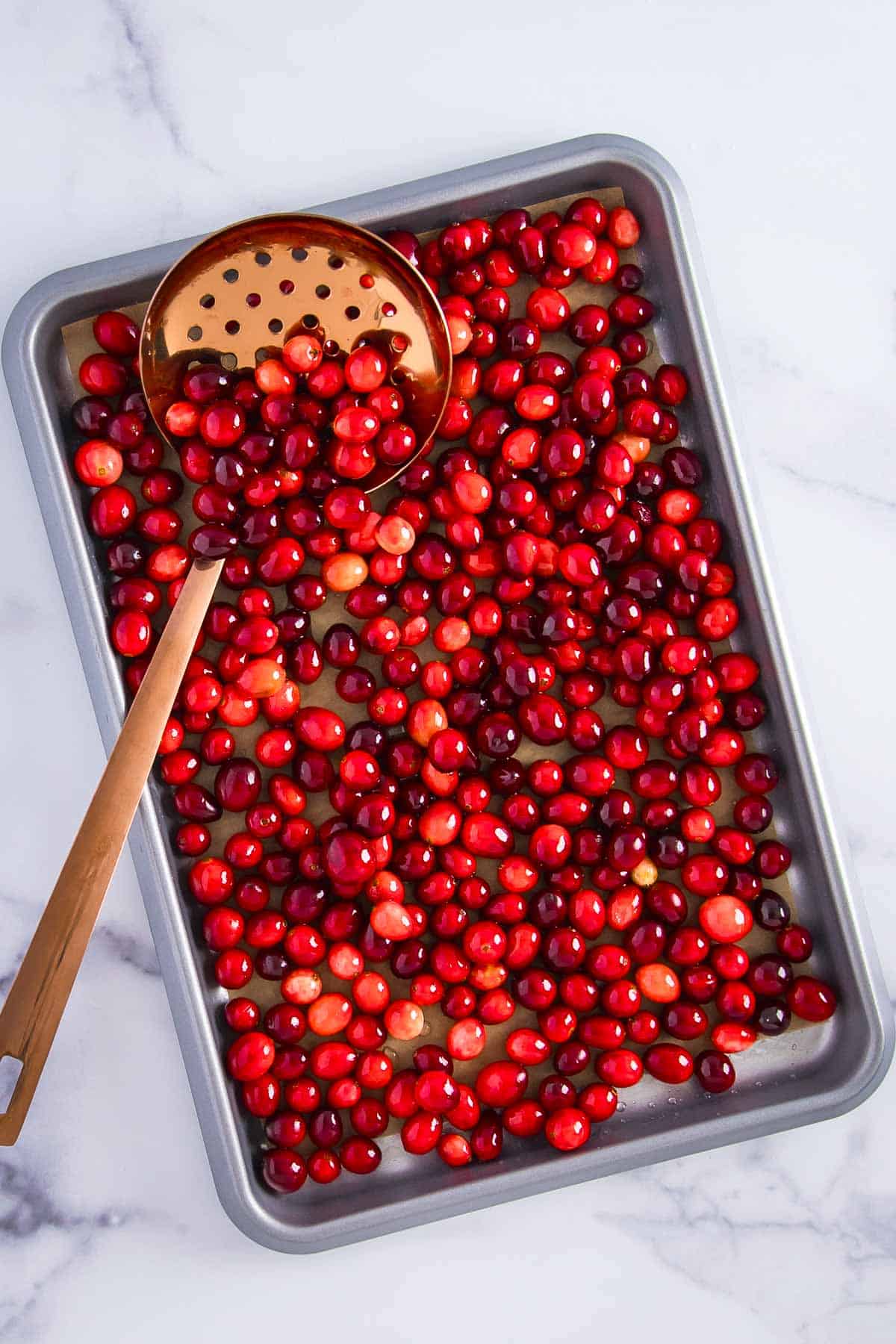 a parchment-lined baking sheet filled with tender cranberries, with a slotted spoon partially filled with cranberries