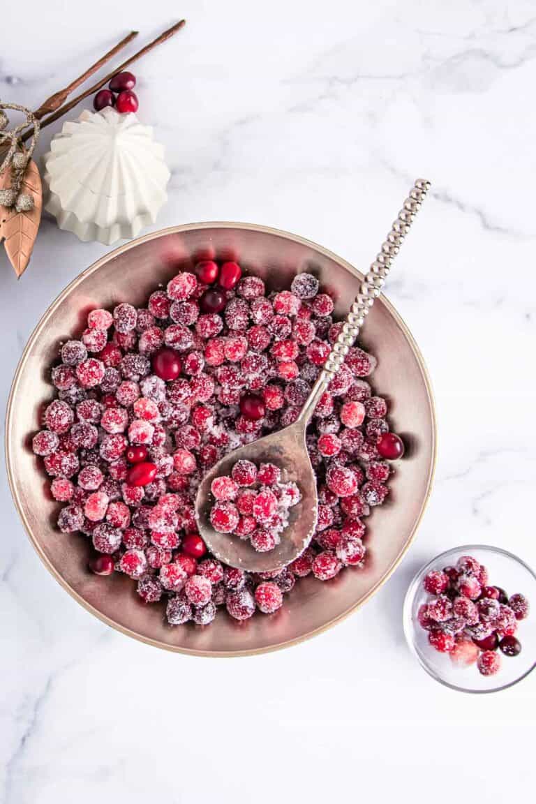 overhead shot of sugared cranberries in a large bowl and some in a small glass bowl; festive decorations beside the large bowl