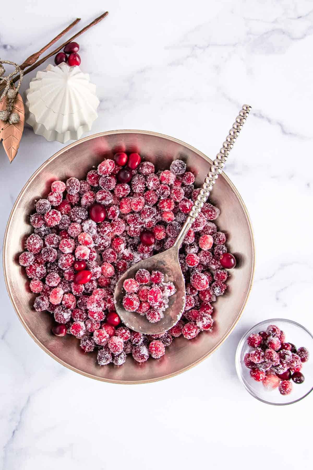 overhead shot of sugared cranberries in a large bowl and some in a small glass bowl; festive decorations beside the large bowl