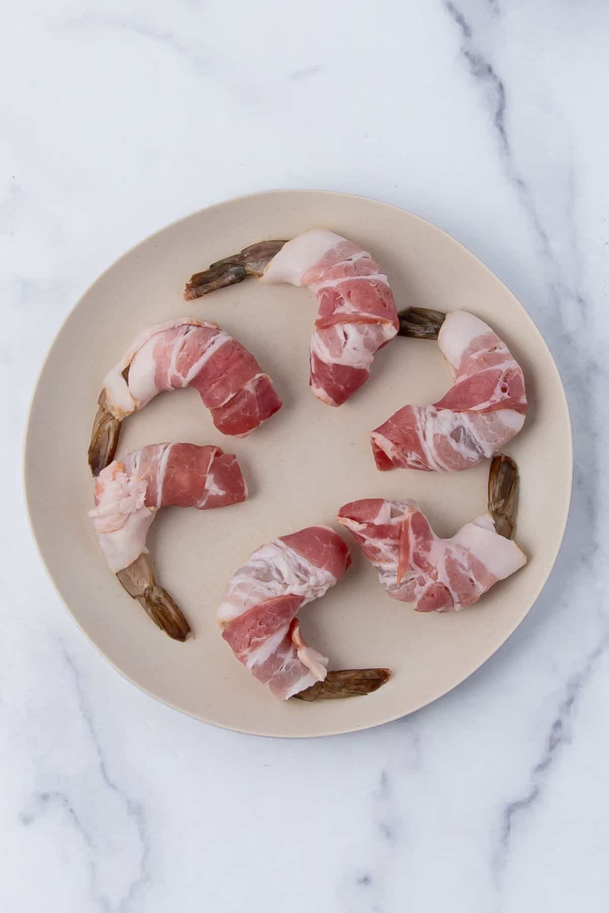 Shrimp wrapped in bacon displayed on a plate, ready for further preparation.