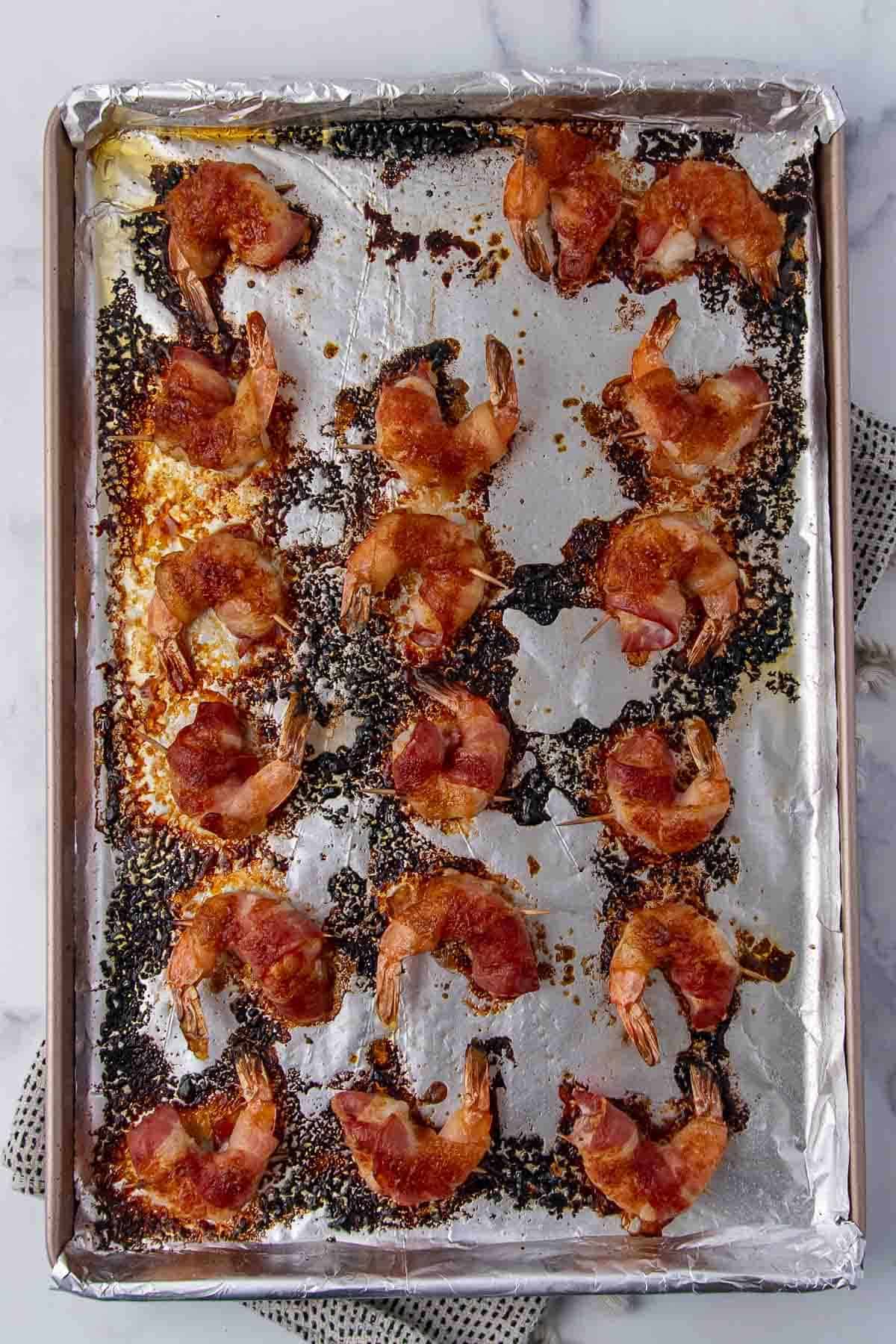 Bacon-wrapped shrimp baked on a foil-lined tray with slightly caramelized edges
