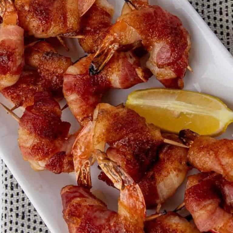 crispy bacon wrapped shrimp with a brown sugar paprika coating on a white plate with a lemon wedge.