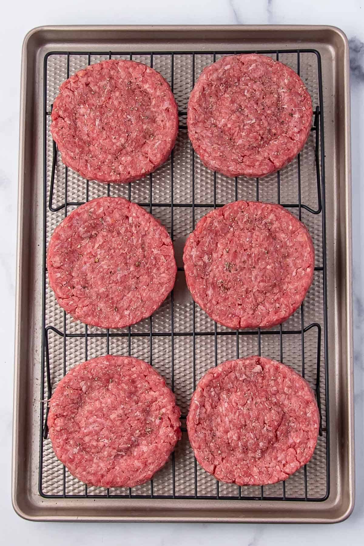 Raw burger patties seasoned and placed on a baking rack ready for the oven.