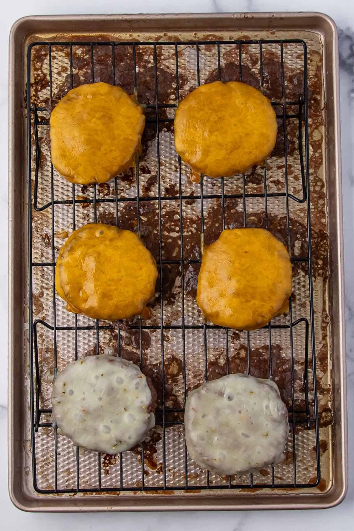 Several cooked patties topped with melted cheese on a baking rack.